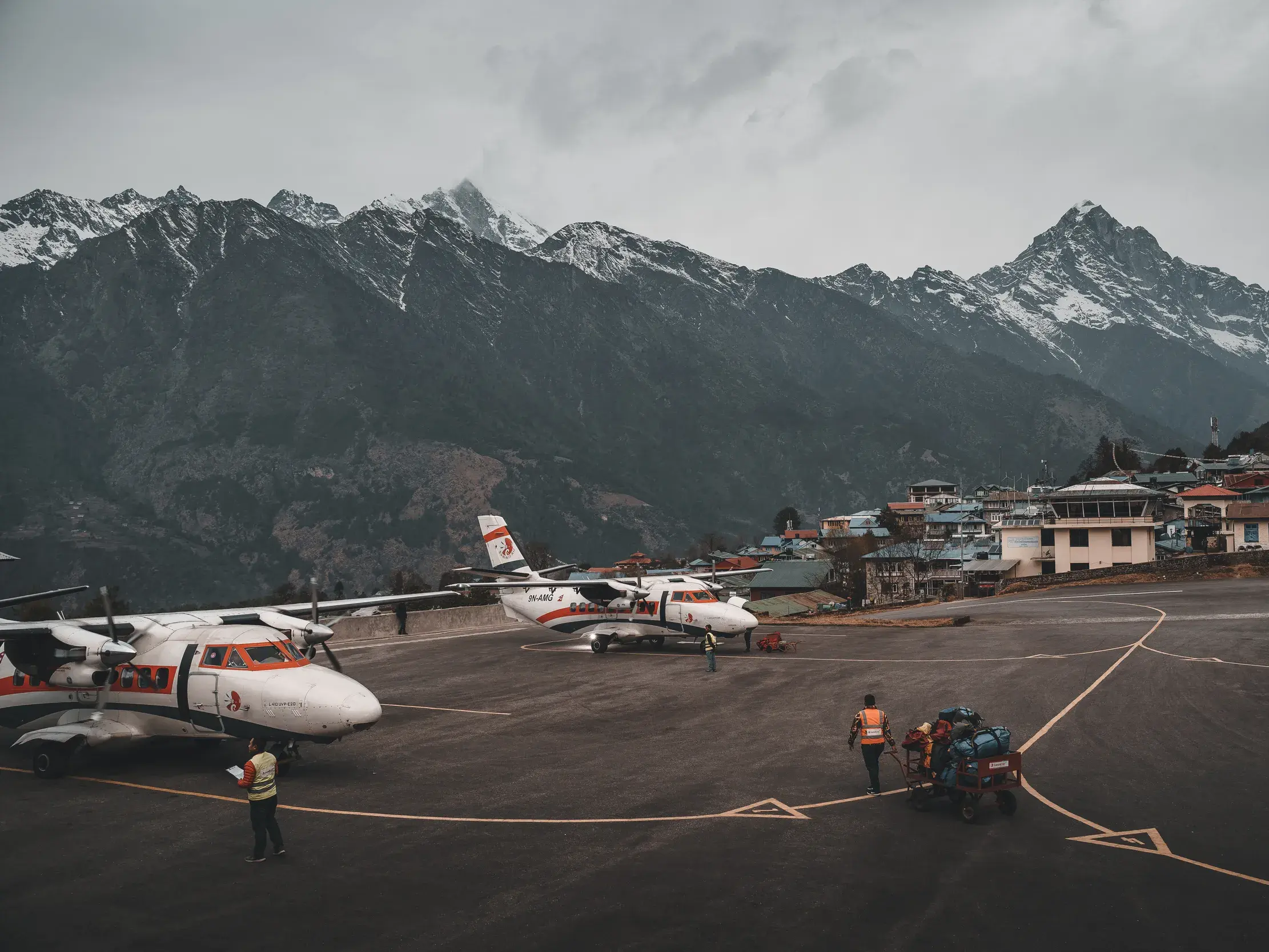 Propellerflugzeuge auf dem Flugfeld in Lukla, wo Trekking-Gepäck verladen wird, vor der beeindruckenden Kulisse des Himalaya.