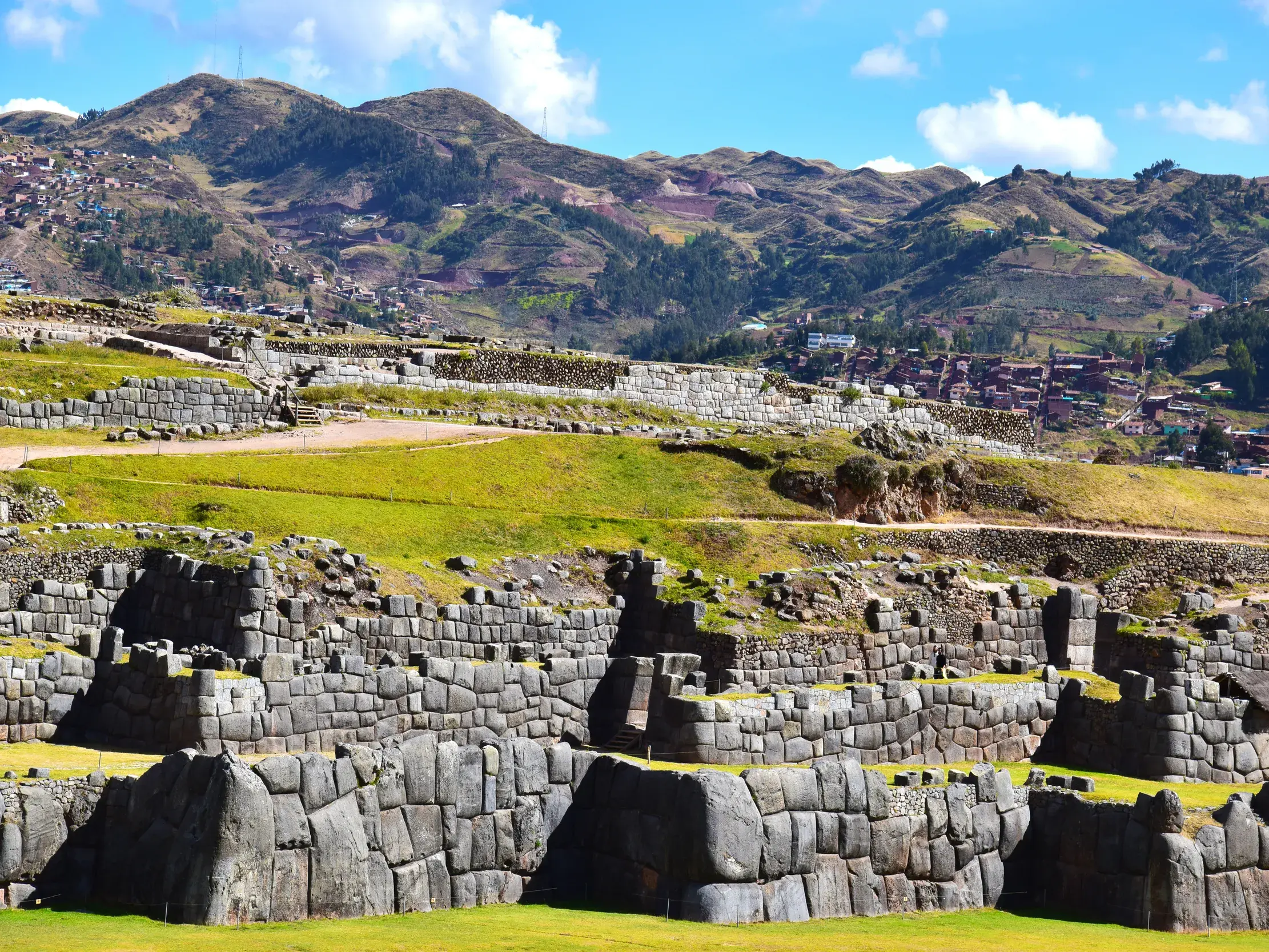 Sonnige Ansicht der terrassierten Inka-Festung Sacasyhuman mit ihren perfekt gefügten Mauern vor der Bergkulisse Cuscos.