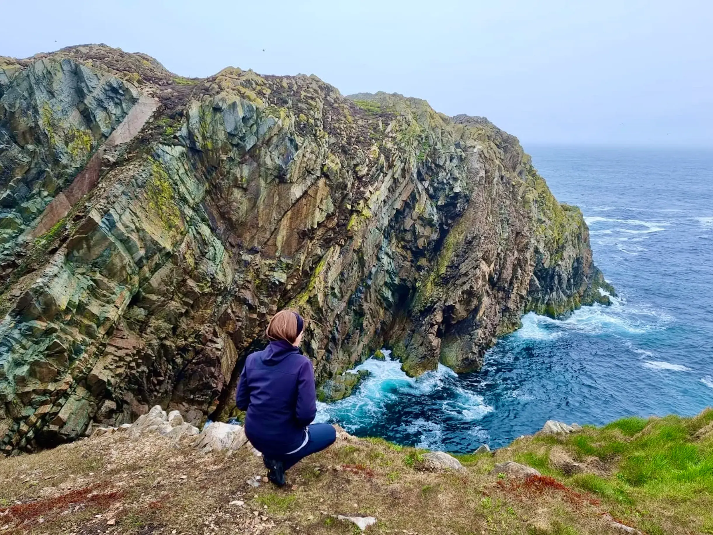 Wanderin genießt auf dem East Coast Trail in Neufundland die Aussicht auf die schroffen, moosbewachsenen Steilklippen.