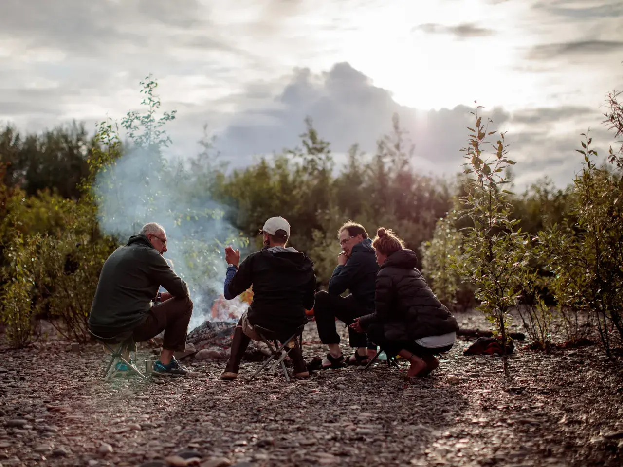 Kleine Reisegruppe entspannt am Lagerfeuer am Ufer des Yukon River nach einem Tag Kanutrekking in der Wildnis Kanadas.