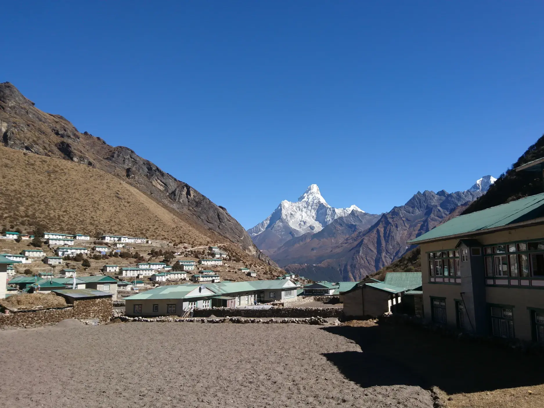 Ein Sherpa-Dorf mit Lodges für Trekking-Gäste im Khumbu-Tal, dahinter ragt der schneebedeckte Ama Dablam in den Himmel.