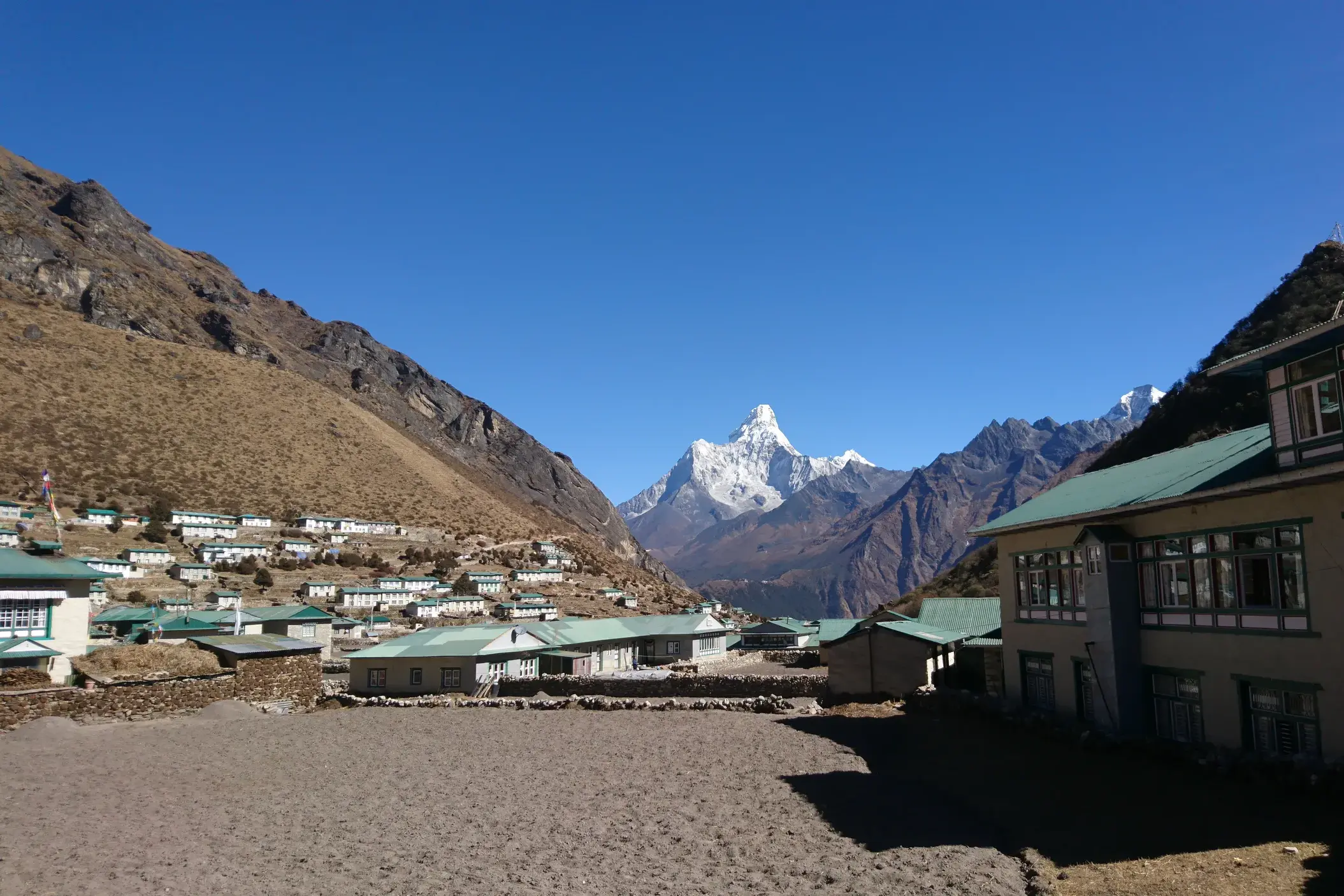 Ein Sherpa-Dorf mit Lodges für Trekking-Gäste im Khumbu-Tal, dahinter ragt der schneebedeckte Ama Dablam in den Himmel.