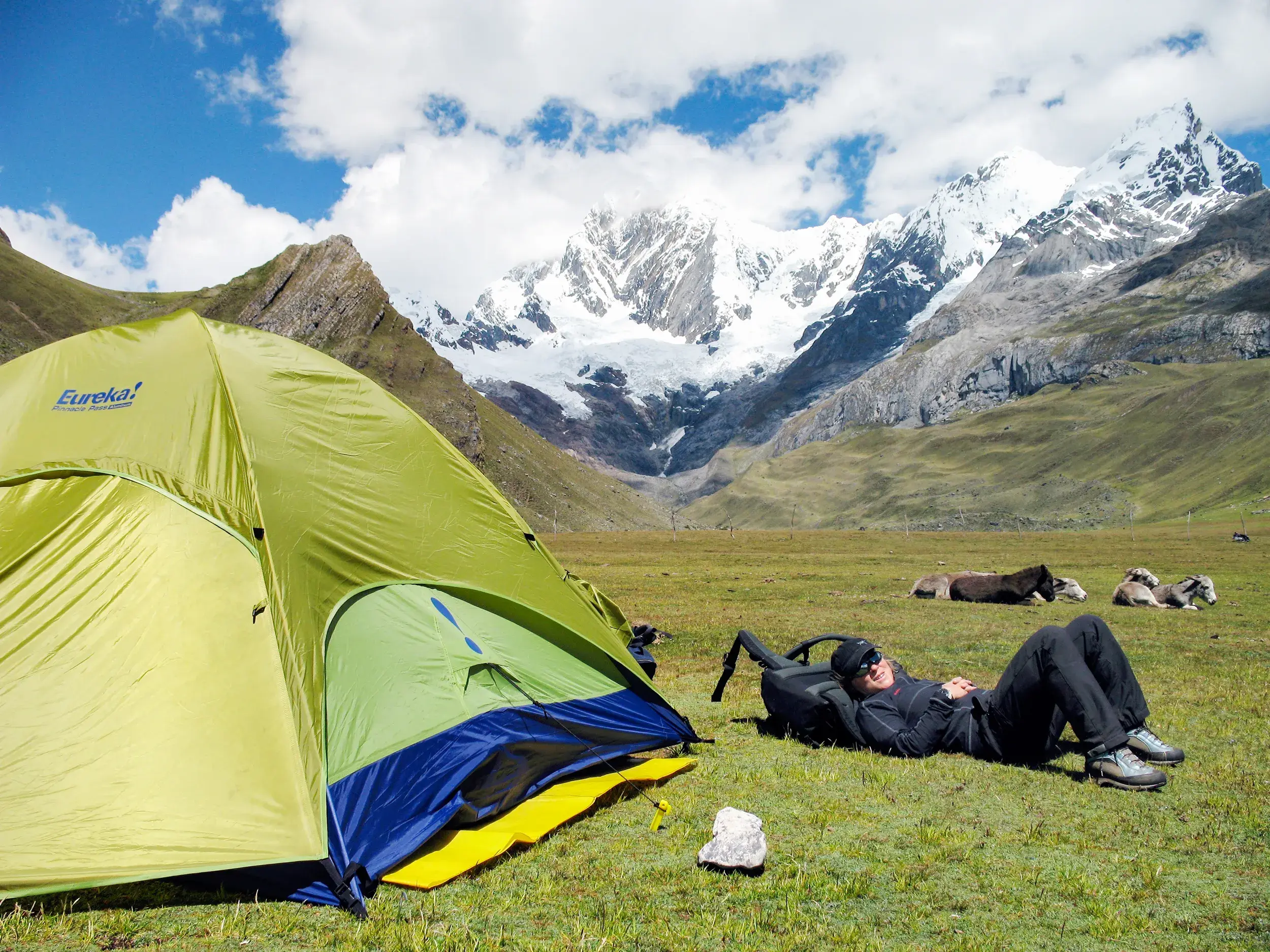 Ein Trekker entspannt auf einer Wiese neben seinem Zelt mit Blick auf die schneebedeckte Bergkette der Cordillera Blanca in Peru.