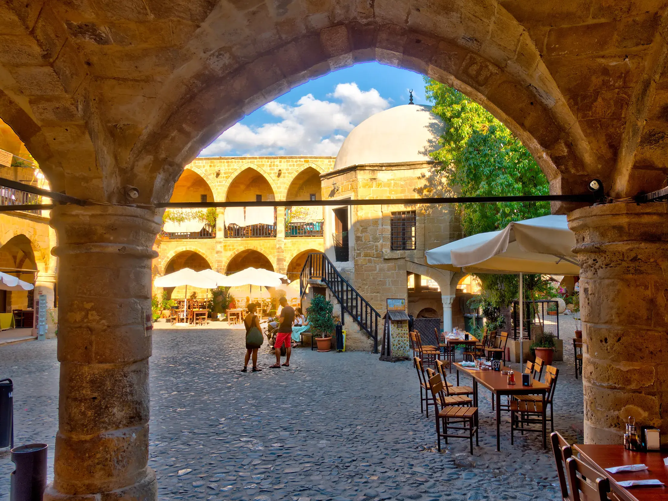 Blick durch steinerne Arkaden in den belebten Innenhof der Karawanserei Büyük Han in Nordnikosia mit vielen Cafés.