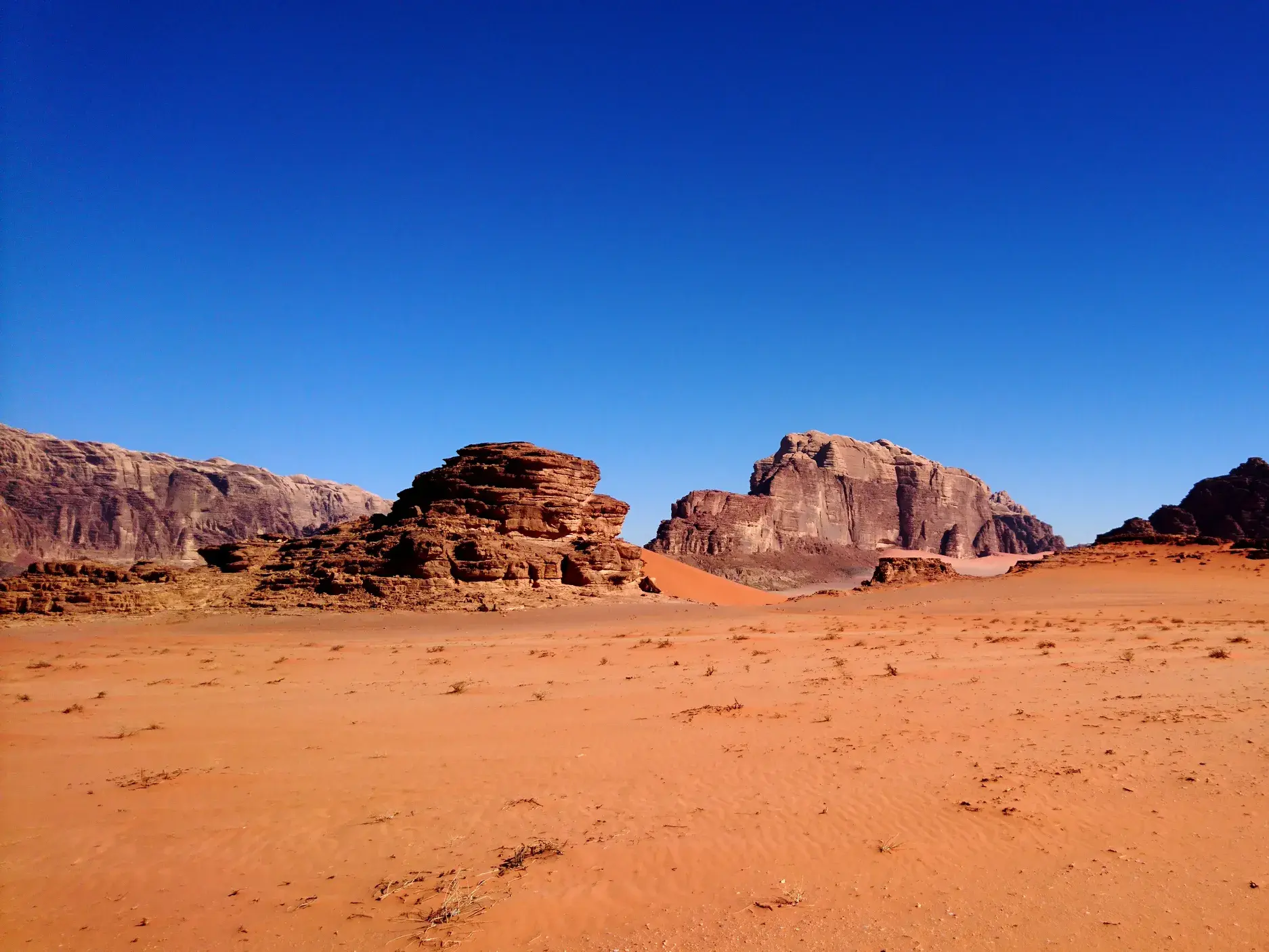 Weite, rote Sandwüste des Wadi Rum in Jordanien mit bizarren Felsformationen unter einem strahlend blauen Himmel.