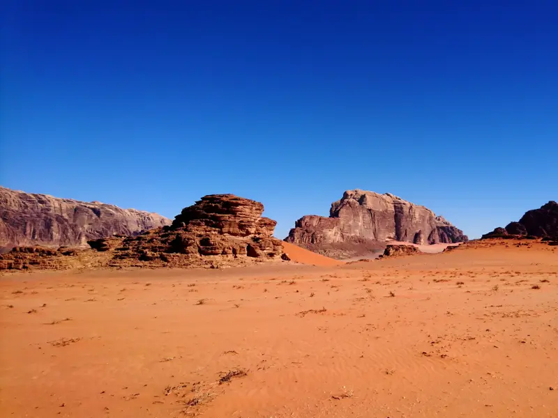 Weite, rote Sandwüste des Wadi Rum in Jordanien mit bizarren Felsformationen unter einem strahlend blauen Himmel.