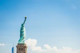 Blick vom Wasser auf die Freiheitsstatue auf Liberty Island mit der Skyline von Lower Manhattan und dem One World Trade Center.