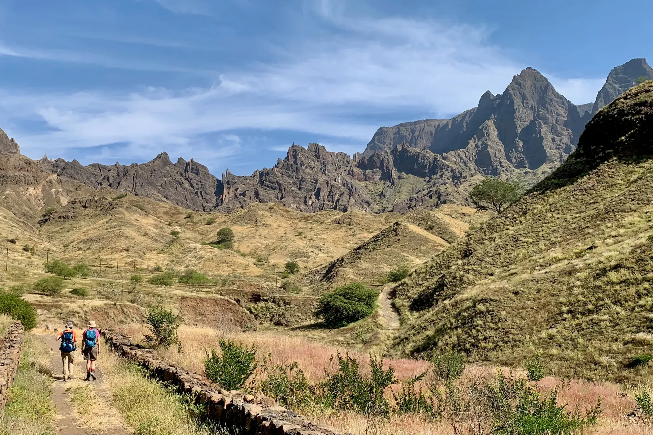 Zwei Trekking-Reisende wandern auf einem Hirtenpfad durch die zerklüftete Vulkanlandschaft der Kapverden-Insel Santo Antão.