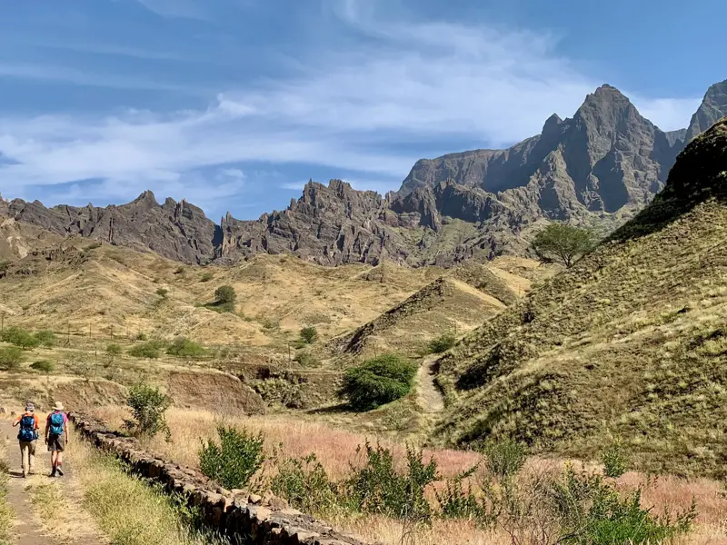 Zwei Trekking-Reisende wandern auf einem Hirtenpfad durch die zerklüftete Vulkanlandschaft der Kapverden-Insel Santo Antão.