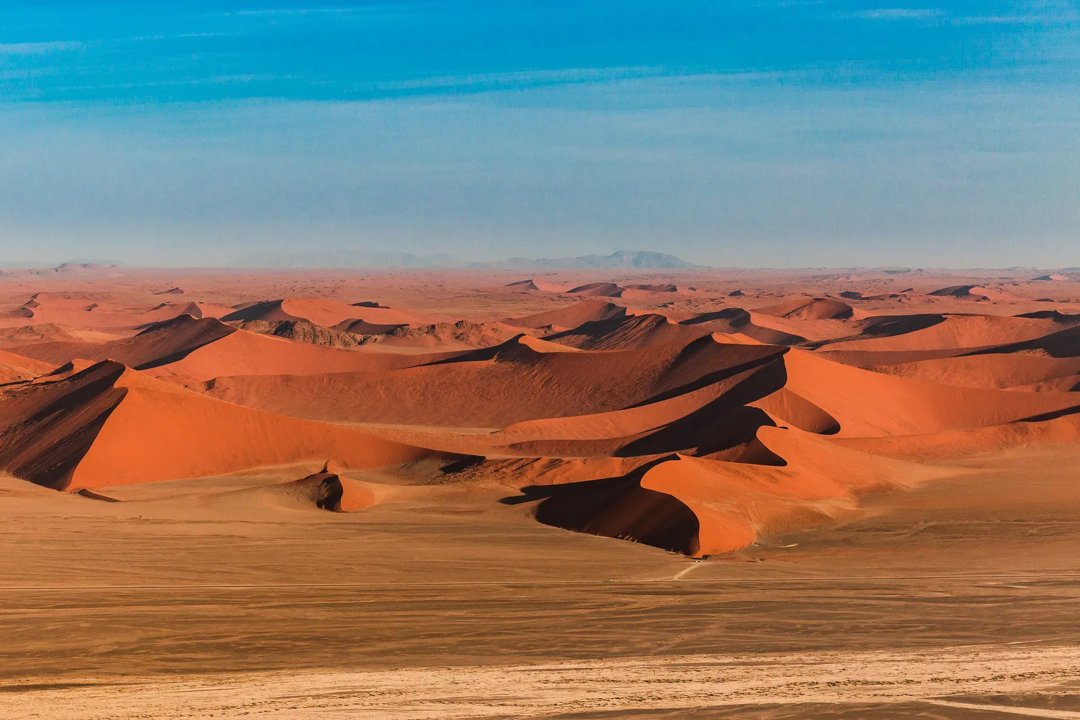 Panoramablick über die leuchtend roten Dünen im Sossusvlei, Namib-Naukluft-Park, die sich unter einem strahlend blauen Himmel erstrecken.