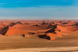 Panoramablick über die leuchtend roten Dünen im Sossusvlei, Namib-Naukluft-Park, die sich unter einem strahlend blauen Himmel erstrecken.