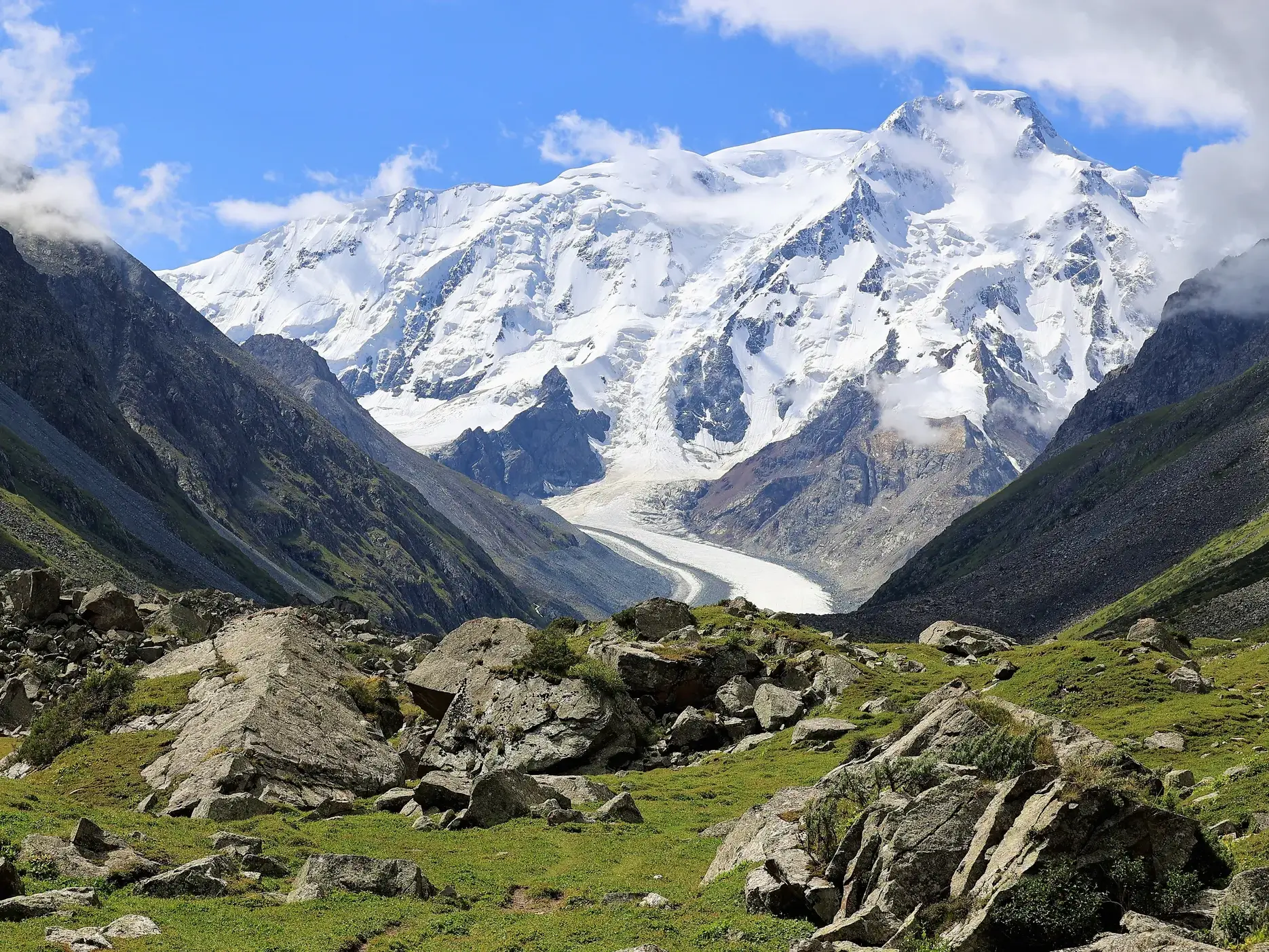Felsige, grüne Bergwiese mit Blick auf den vergletscherten Gipfel des Karakol Peak im Terskej-Alatau-Gebirge.