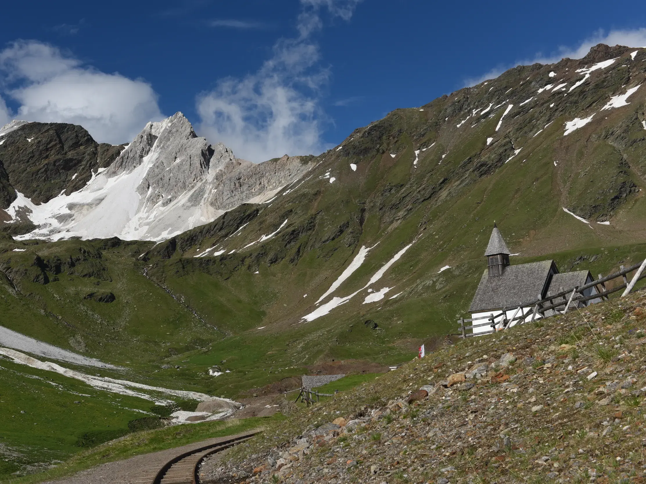 Historische Knappenkapelle und alte Gleise einer Grubenbahn inmitten der grünen Berglandschaft der Zillertaler Alpen.