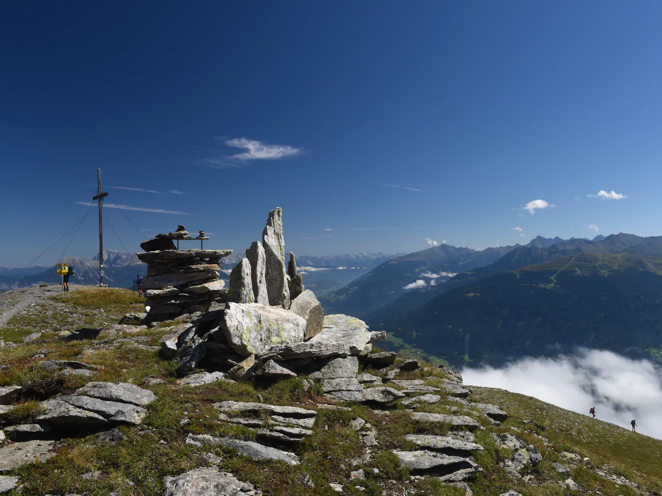 Wanderer am Steinmann auf dem Gipfel des Krahberg mit Panoramablick über die Alpentäler bei der E5 Alpenüberquerung.