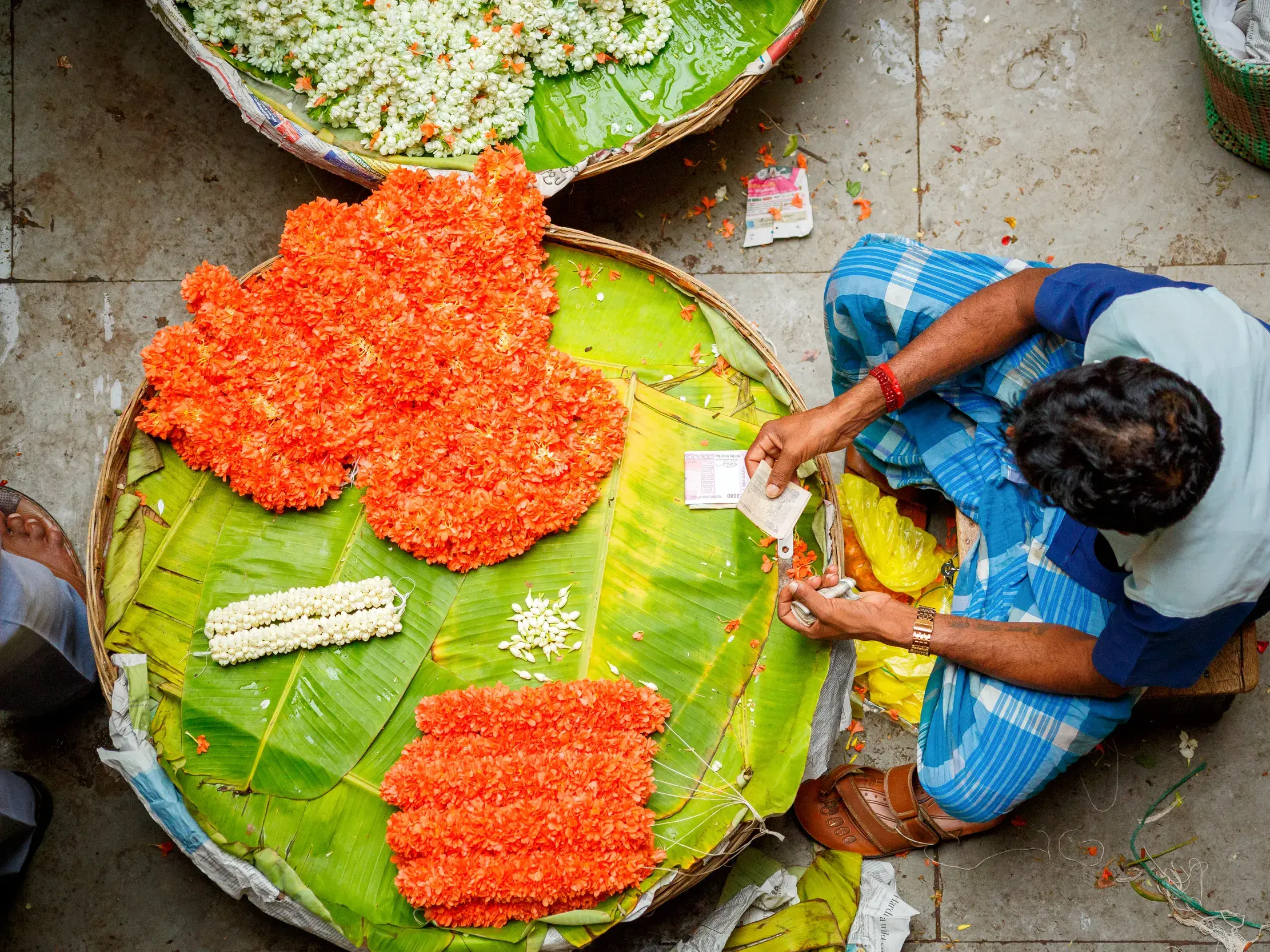 Vogelperspektive eines Verkäufers, der auf dem Devaraja-Markt in Mysore leuchtend orange Blumengirlanden anordnet.