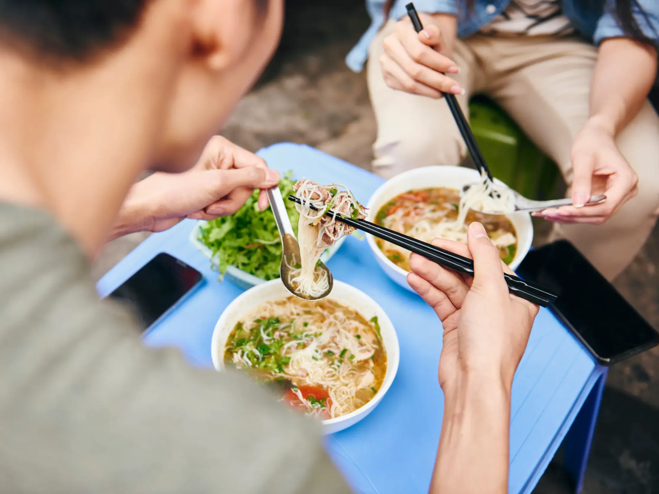 Zwei Teilnehmer einer Studiosus Rundreise genießen eine traditionelle vietnamesische Nudelsuppe mit frischen Kräutern in Hanoi.