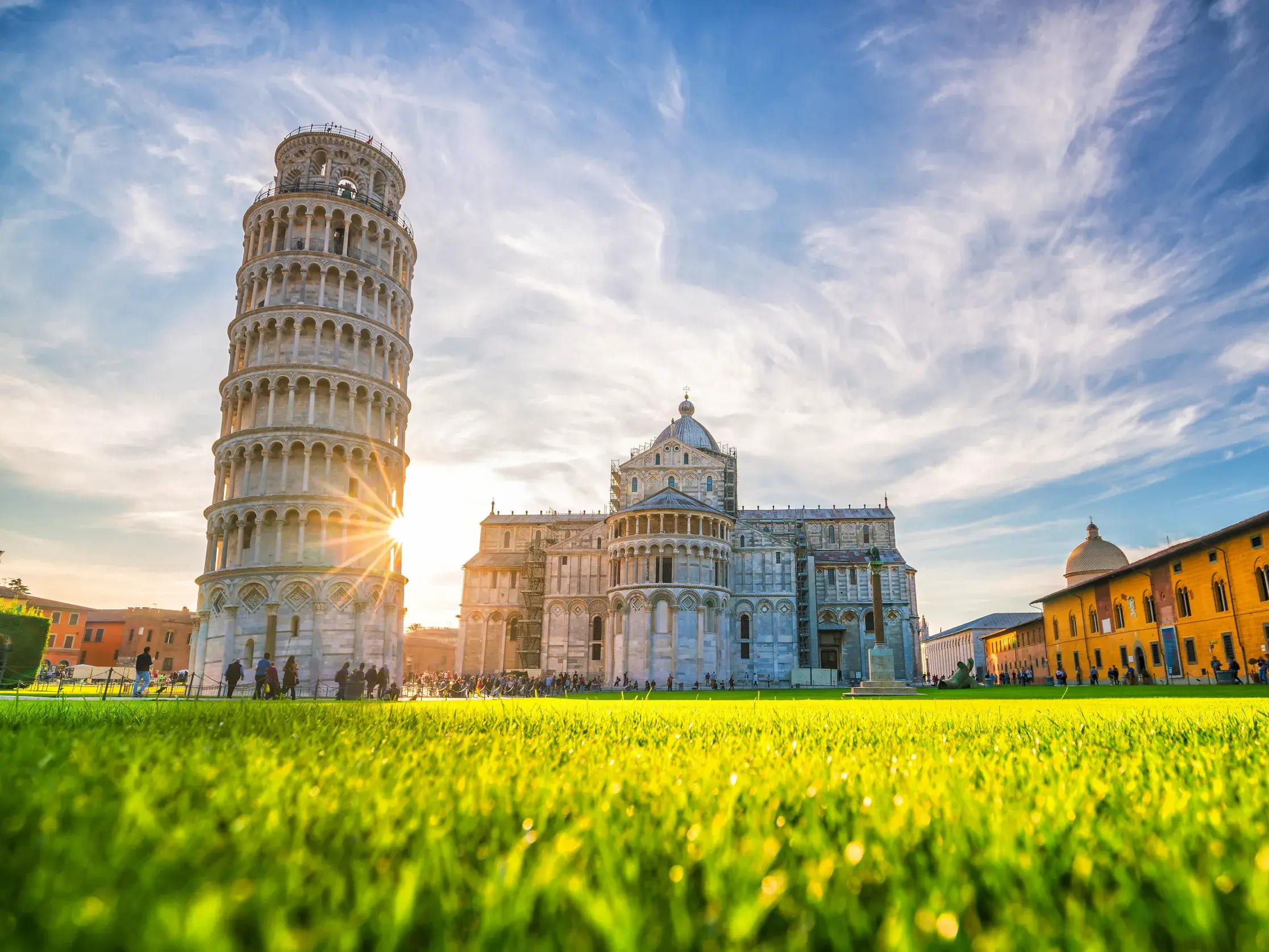 Der Schiefe Turm von Pisa und der Dom auf dem Platz der Wunder, von einer Wiese aus in der tiefstehenden Sonne fotografiert.