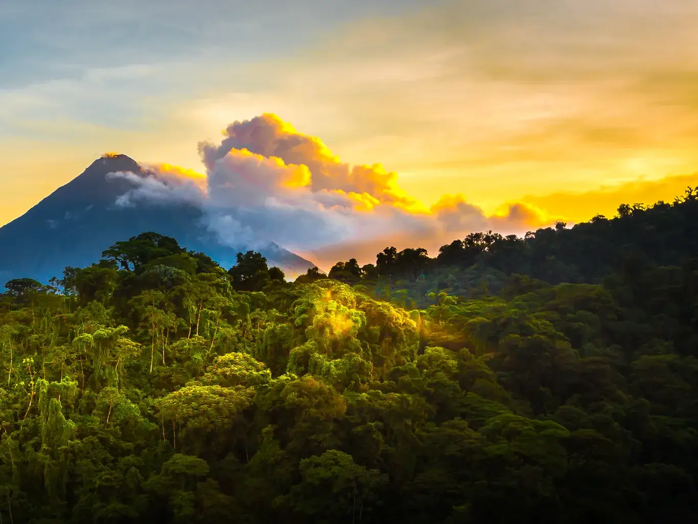 Der Vulkan Arenal ragt bei Sonnenuntergang über den dichten, grünen Regenwald von Costa Rica nahe La Fortuna.