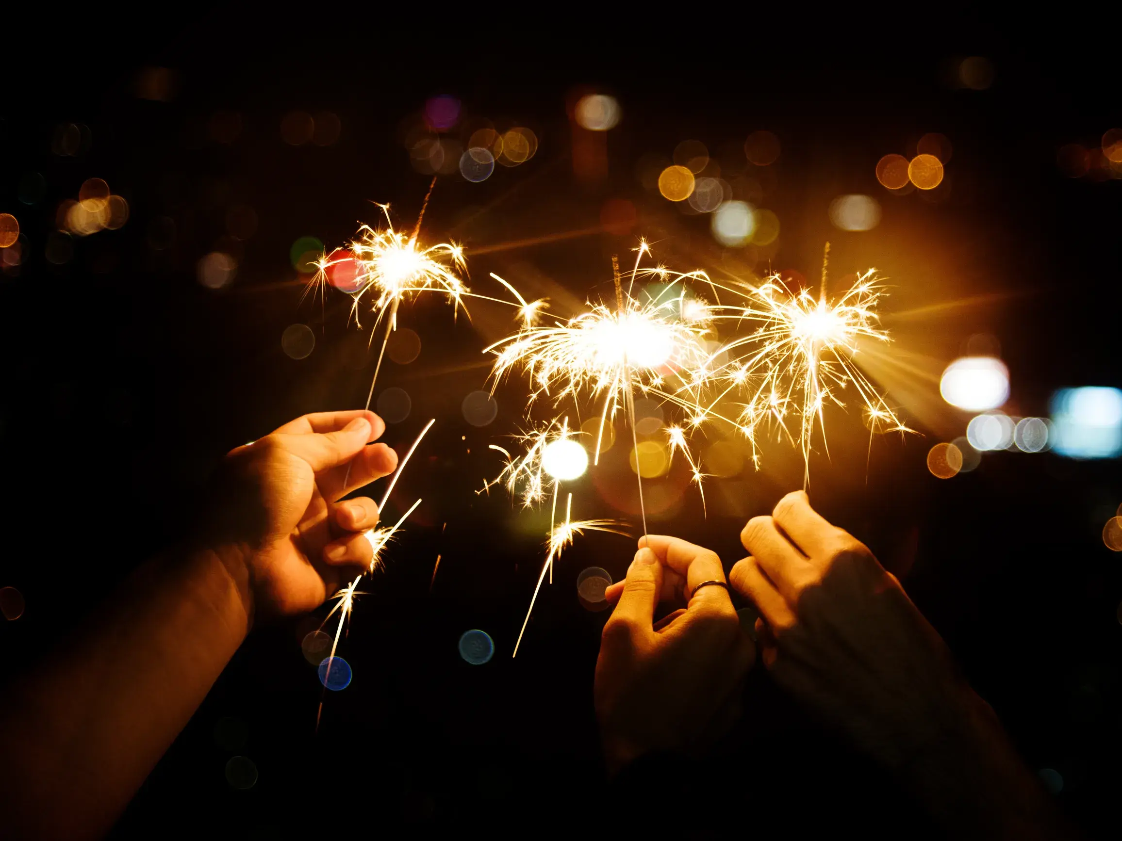Gemeinsames Feiern bei einer Singlereise: Hände halten funkelnde Wunderkerzen in der Silvesternacht in Helsinki.