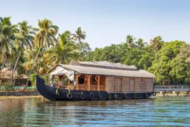 Ein traditionelles Hausboot ankert in der Lagunenlandschaft der Kerala Backwaters in Südindien, im Hintergrund ragen hohe Palmen auf.