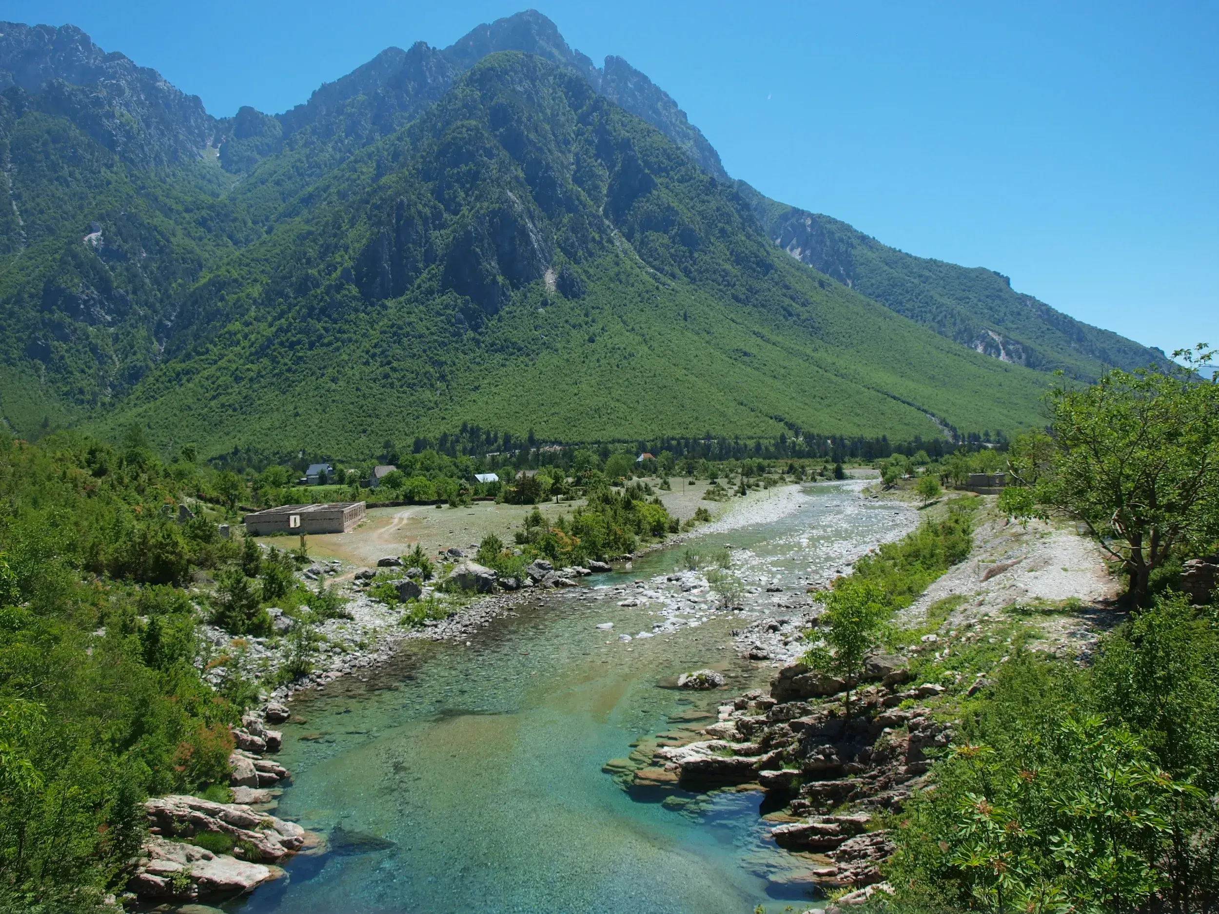 Blick auf den türkisfarbenen Fluss im Valbona-Tal, umgeben von den grünen, majestätischen Gipfeln der Albanischen Alpen.