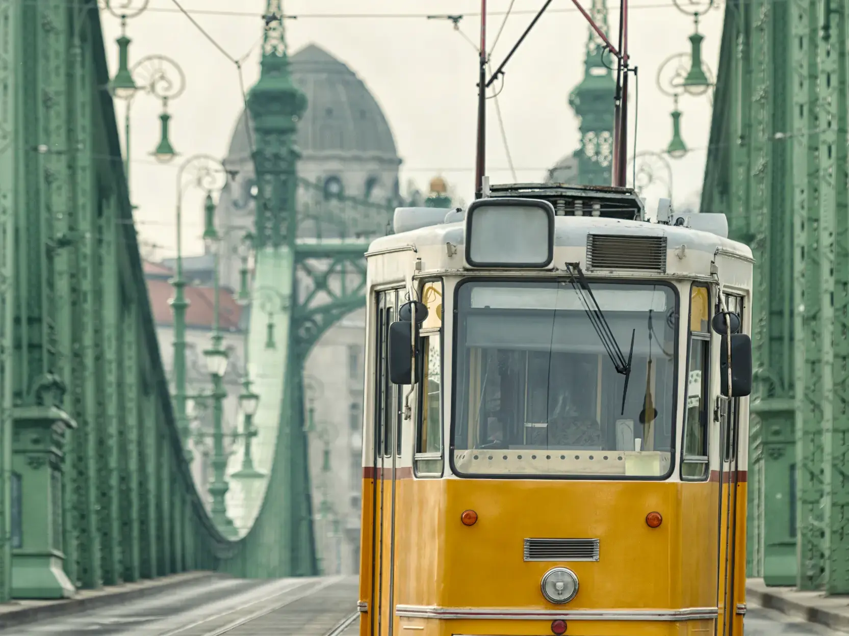 Eine gelbe, historische Straßenbahn überquert die Kettenbrücke in Budapest mit Blick in Richtung Gellertberg.