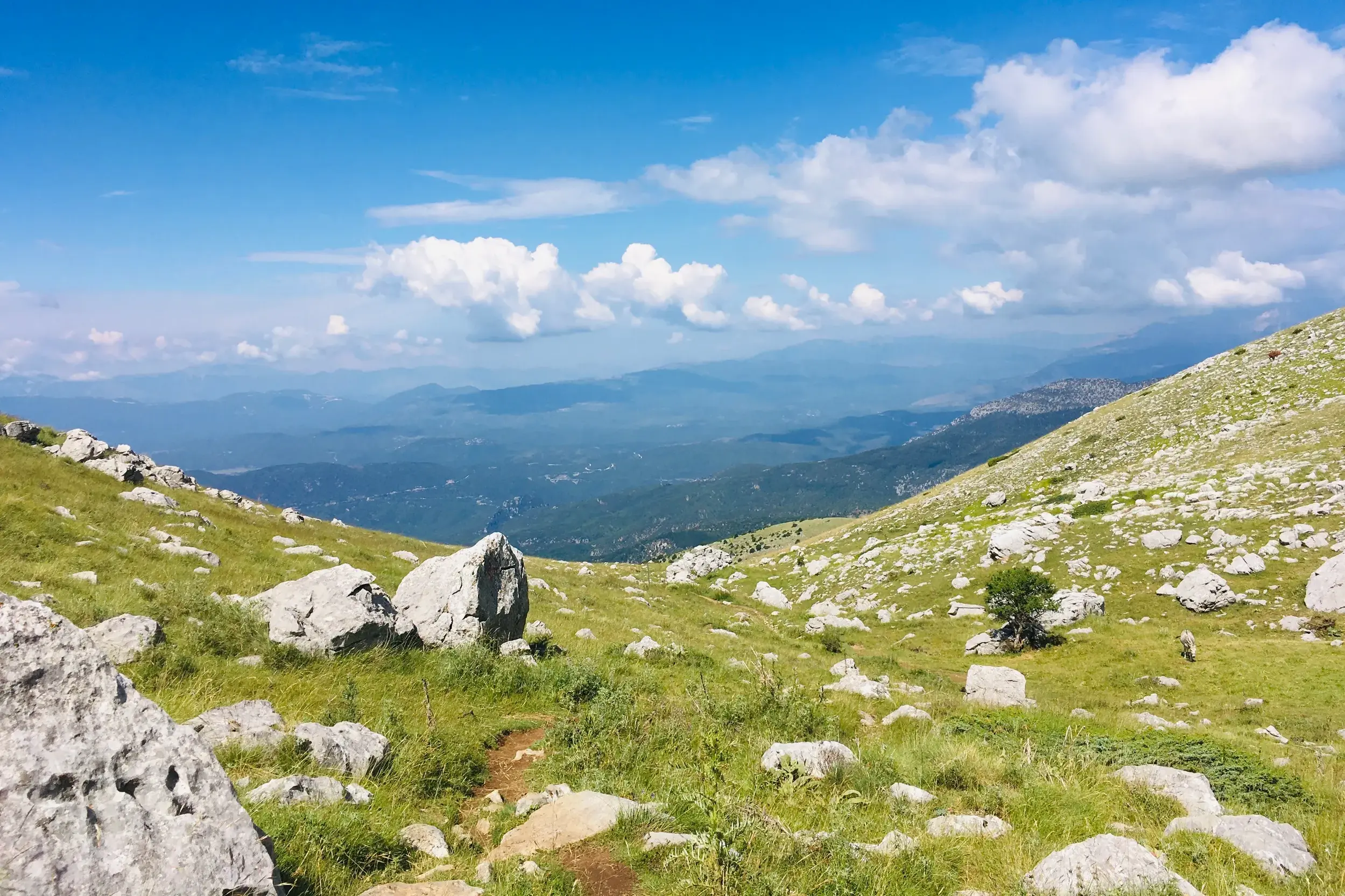 Ein schmaler Trampelpfad führt auf einer Trekking-Tour durch die alpine Landschaft der Astrakas-Hochebene in der Zagori-Region.