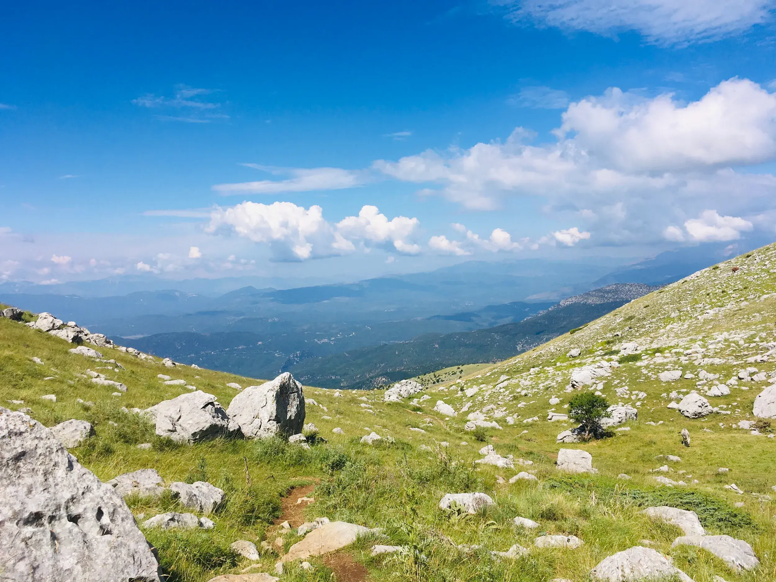 Ein schmaler Trampelpfad führt auf einer Trekking-Tour durch die alpine Landschaft der Astrakas-Hochebene in der Zagori-Region.