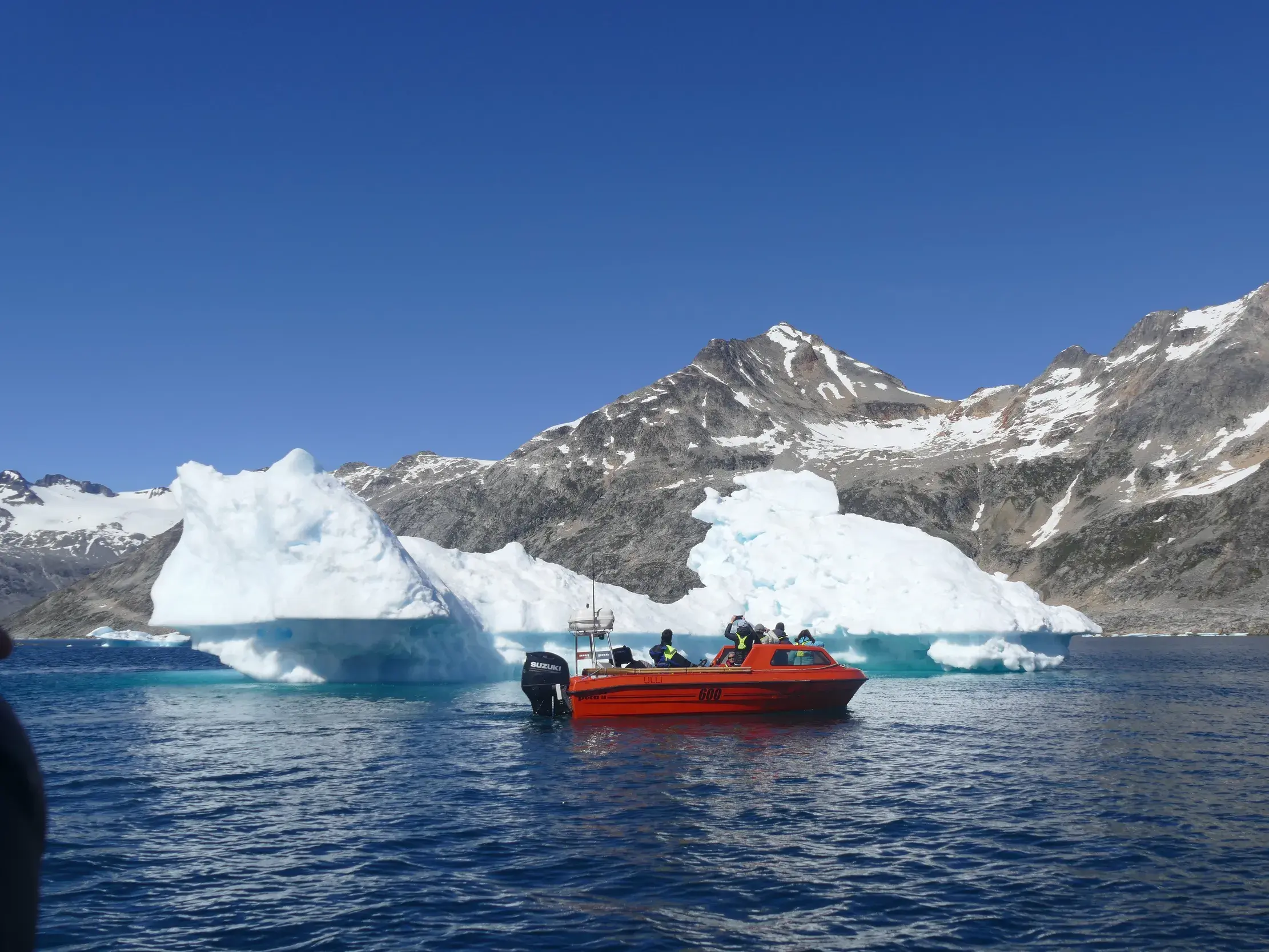 Rotes Boot mit einer Hauser-Reisegruppe an einem treibenden Eisberg im Polarmeer vor der Küste Ostgrönlands.