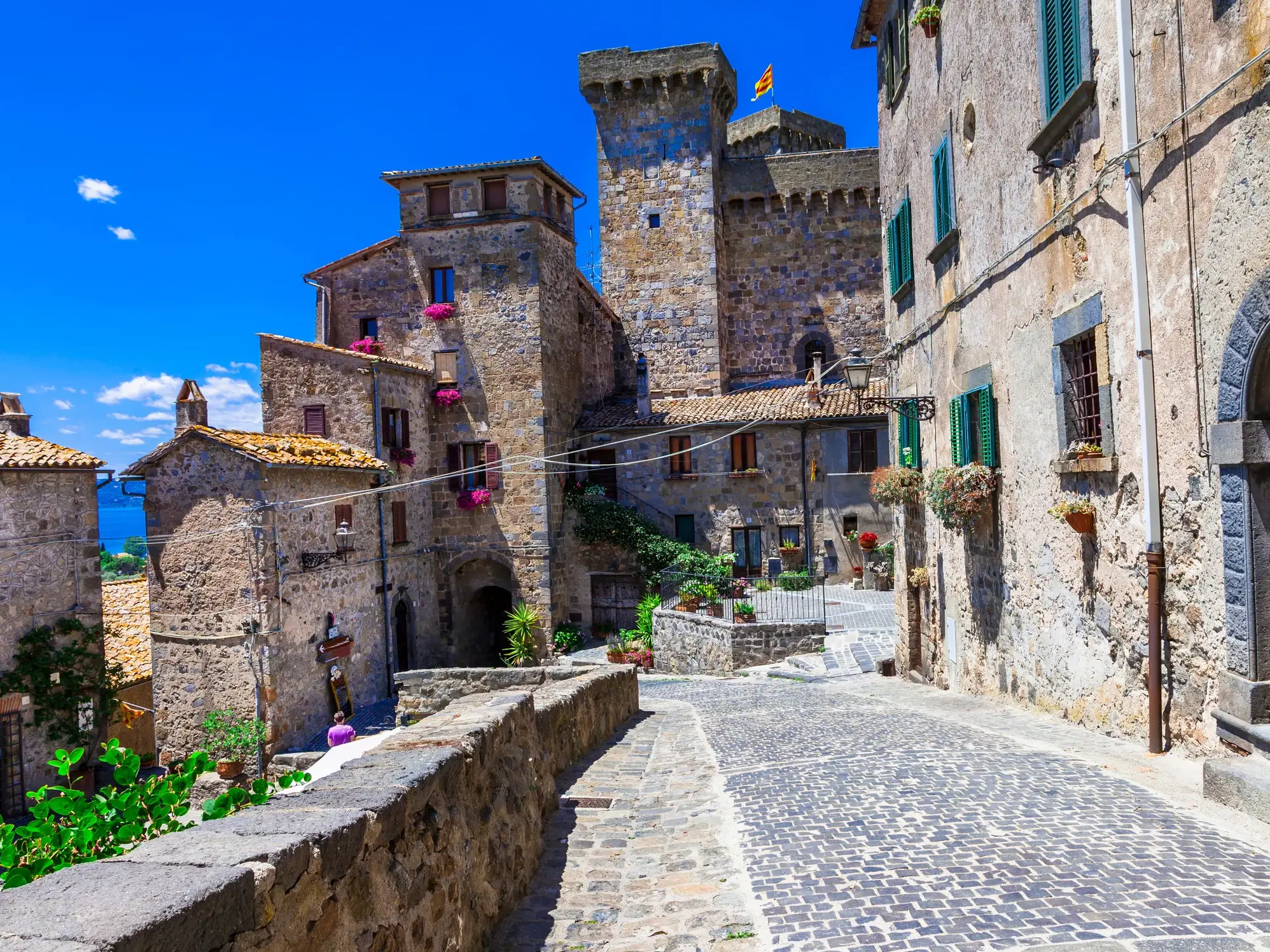 Sonnige, kopfsteingepflasterte Gasse in der Altstadt von Bolsena mit historischen Steinhäusern und Blick auf den Bolsenasee.