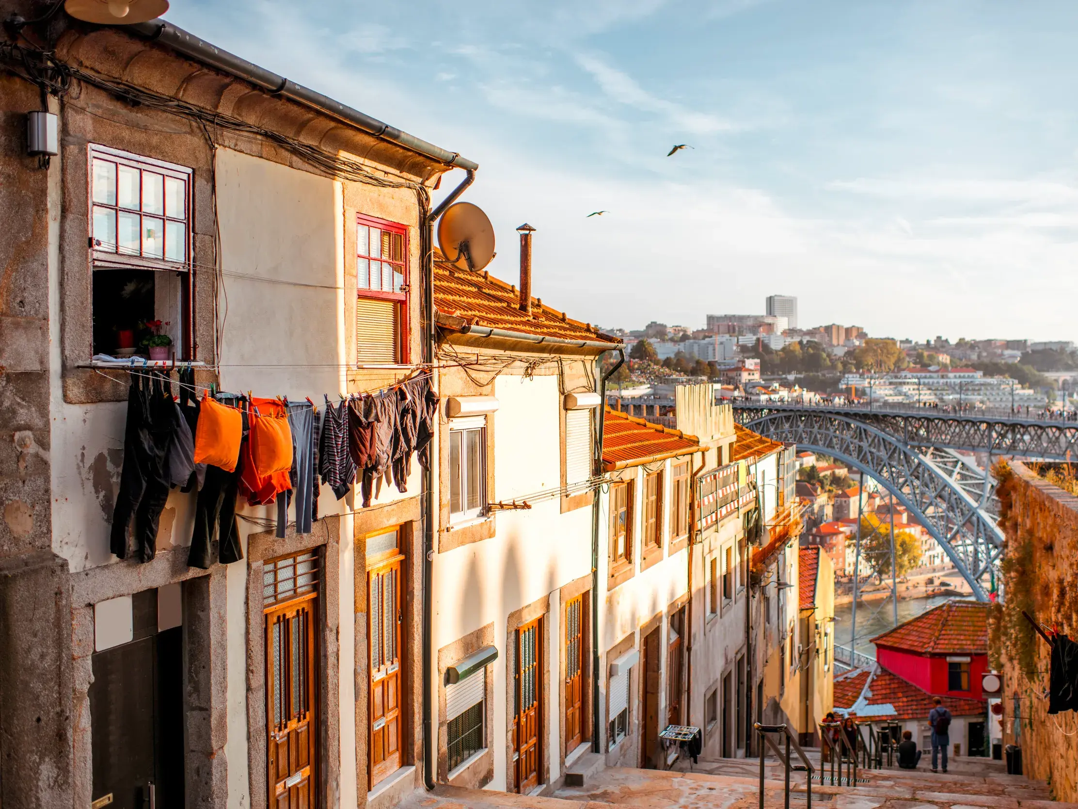 Enge Gasse mit Wäscheleine im Ribeira-Viertel von Porto, mit Blick auf den Fluss Douro und die bekannte Bogenbrücke.