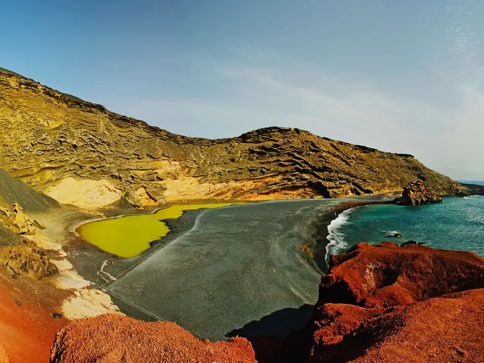 Panoramablick von roten Vulkanfelsen auf den blauen Atlantik und die grüne Lagune Charco de los Clicos bei El Golfo.