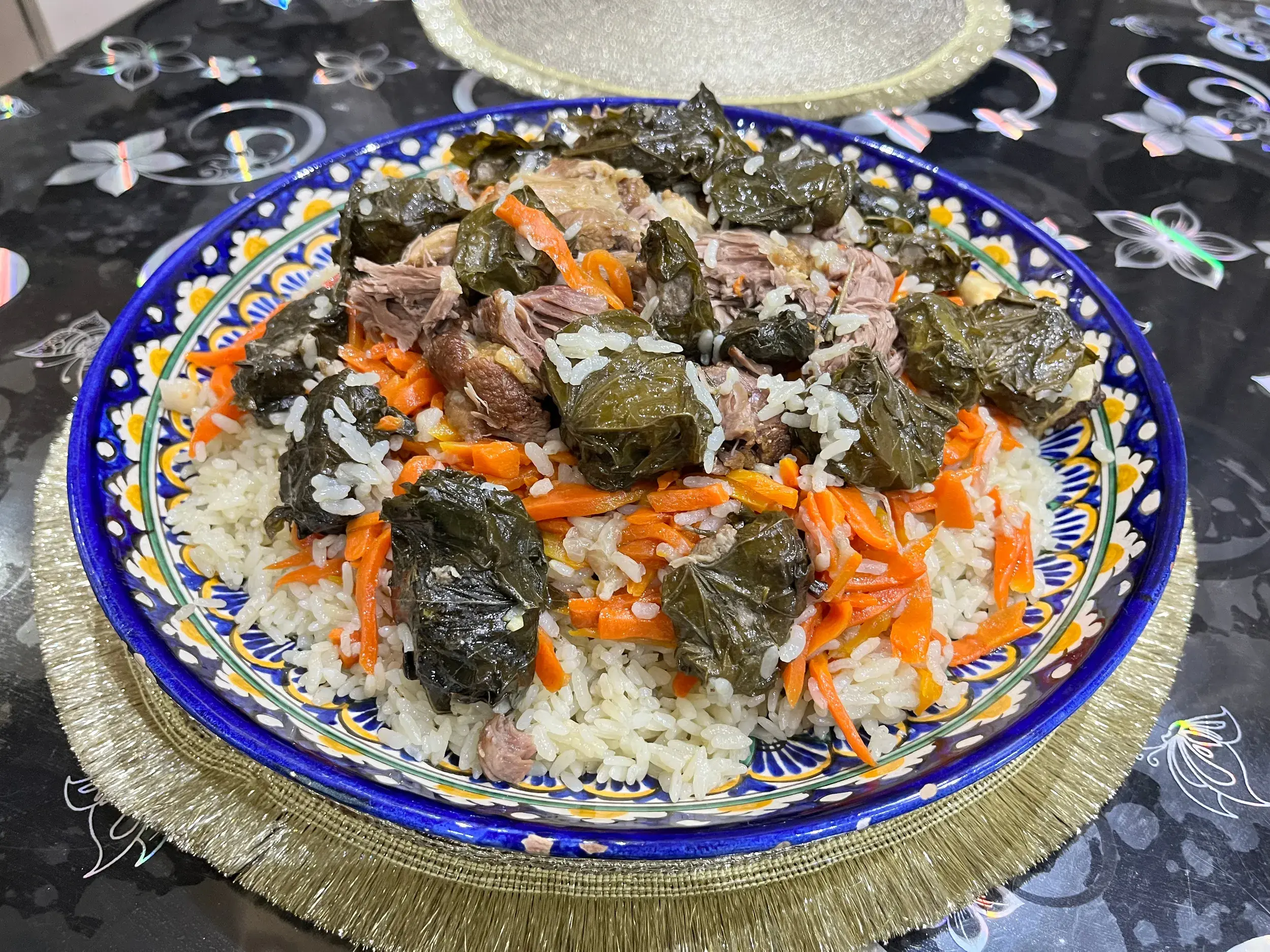 Traditionelles tadschikisches Gericht mit Reis, Karotten und gefüllten Weinblättern, angerichtet auf einem bunten Keramikteller.