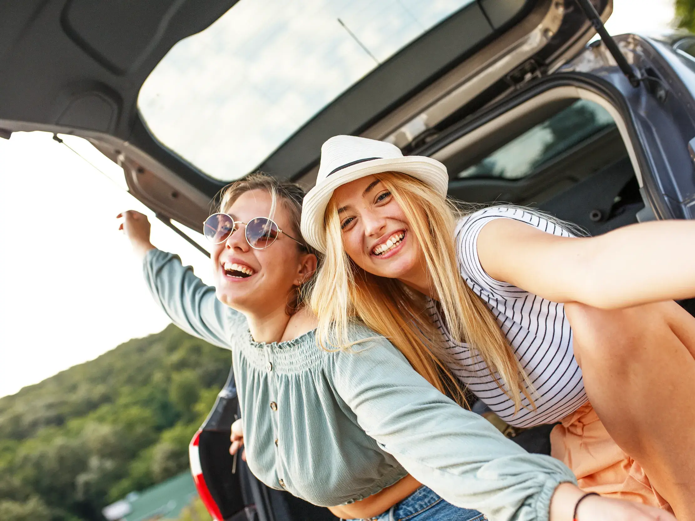 Zwei lachende Freundinnen machen ein Selfie im Kofferraum ihres Mietwagens während ihrer Selbstfahrer-Rundreise auf La Réunion.