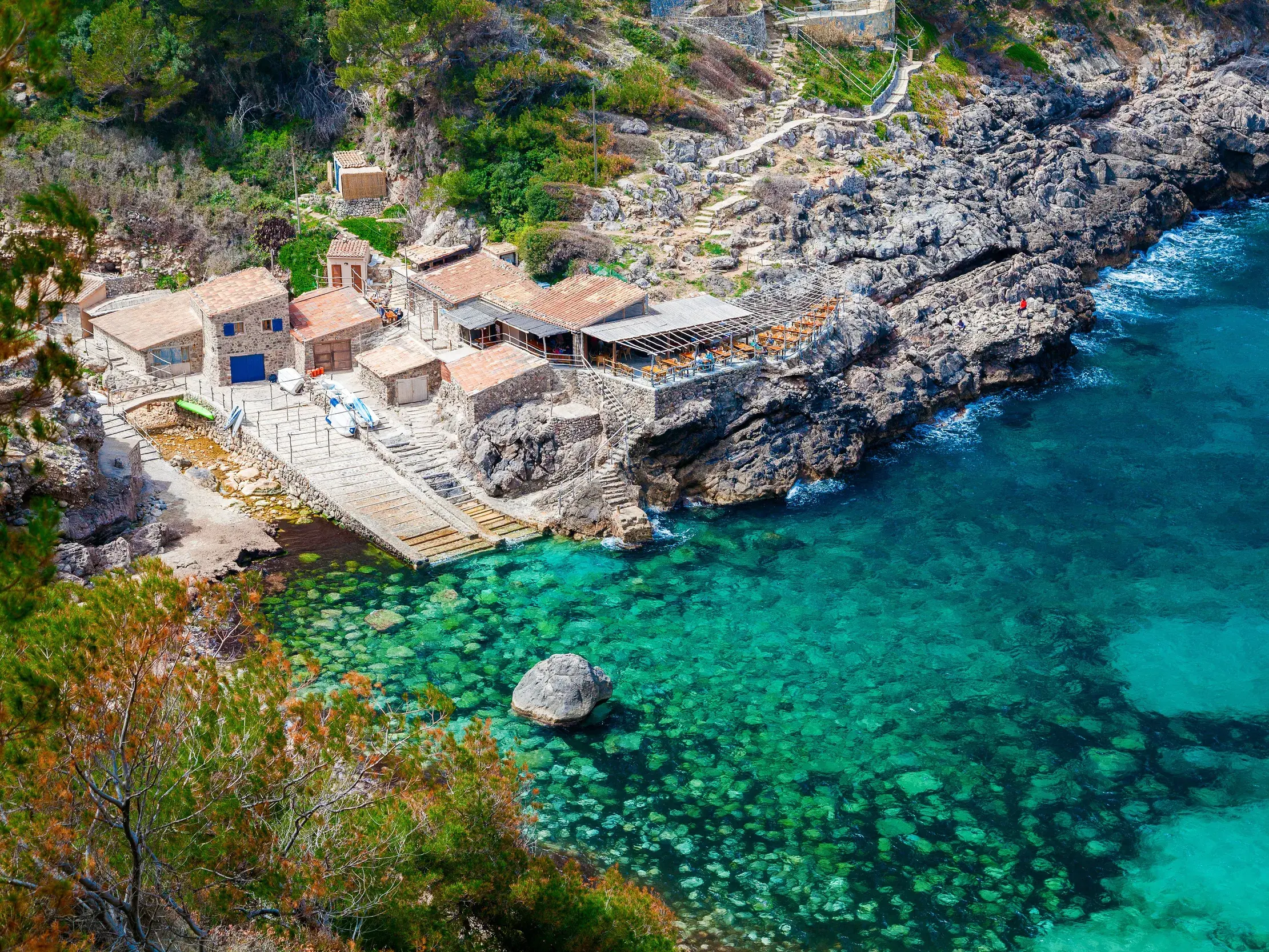 Malerische Steinhäuser in der Felsenbucht Cala Deià mit türkisblauem Wasser in der Serra de Tramuntana auf Mallorca.