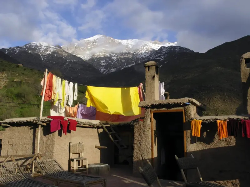 Bunte Wäsche trocknet auf der Lehm-Dachterrasse eines Berberdorfs mit Blick auf den schneebedeckten Djebel Toubkal.
