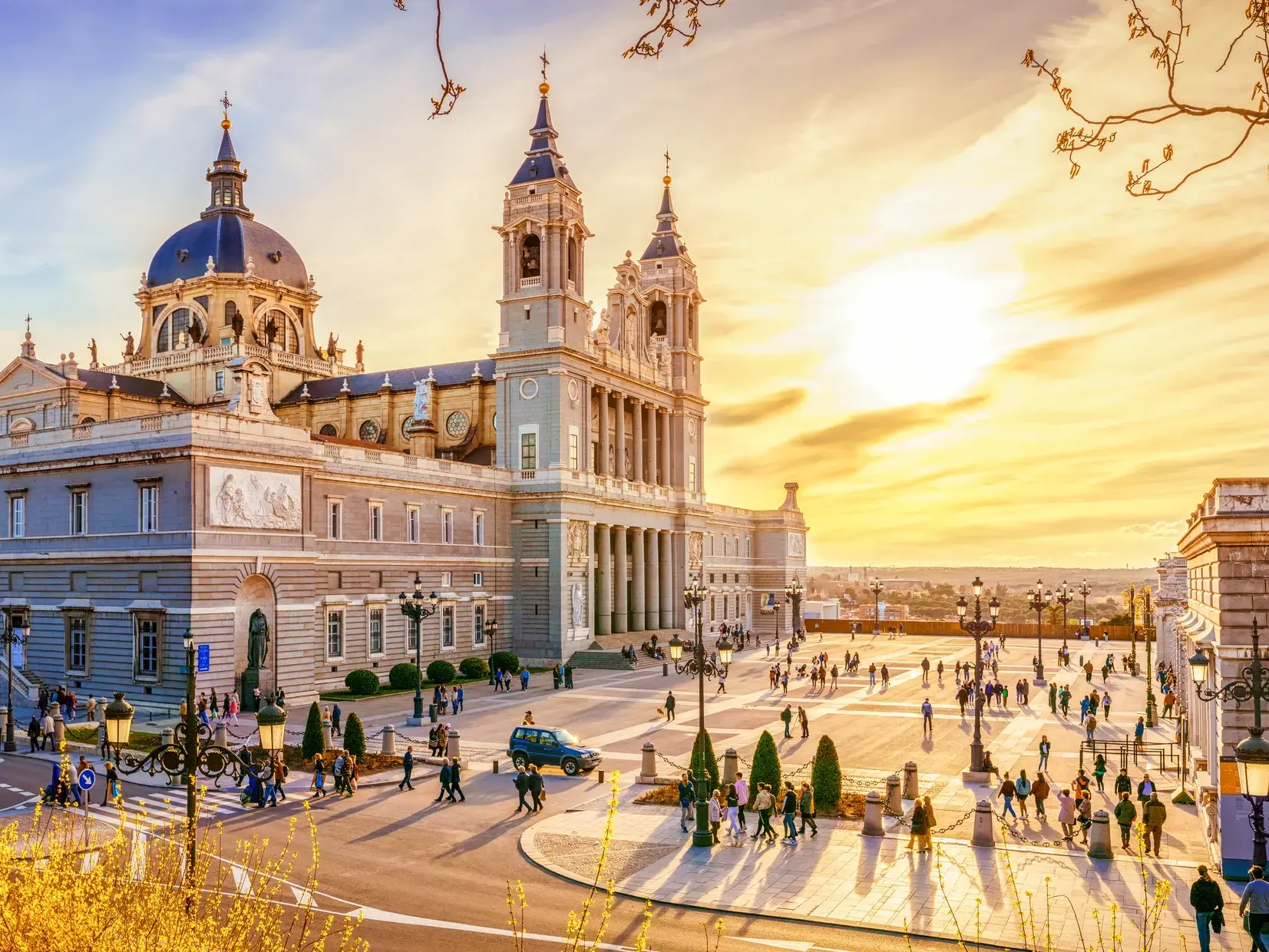 Menschen flanieren vor der Almudena-Kathedrale in Madrid, die von der Abendsonne in goldenes Licht getaucht wird.