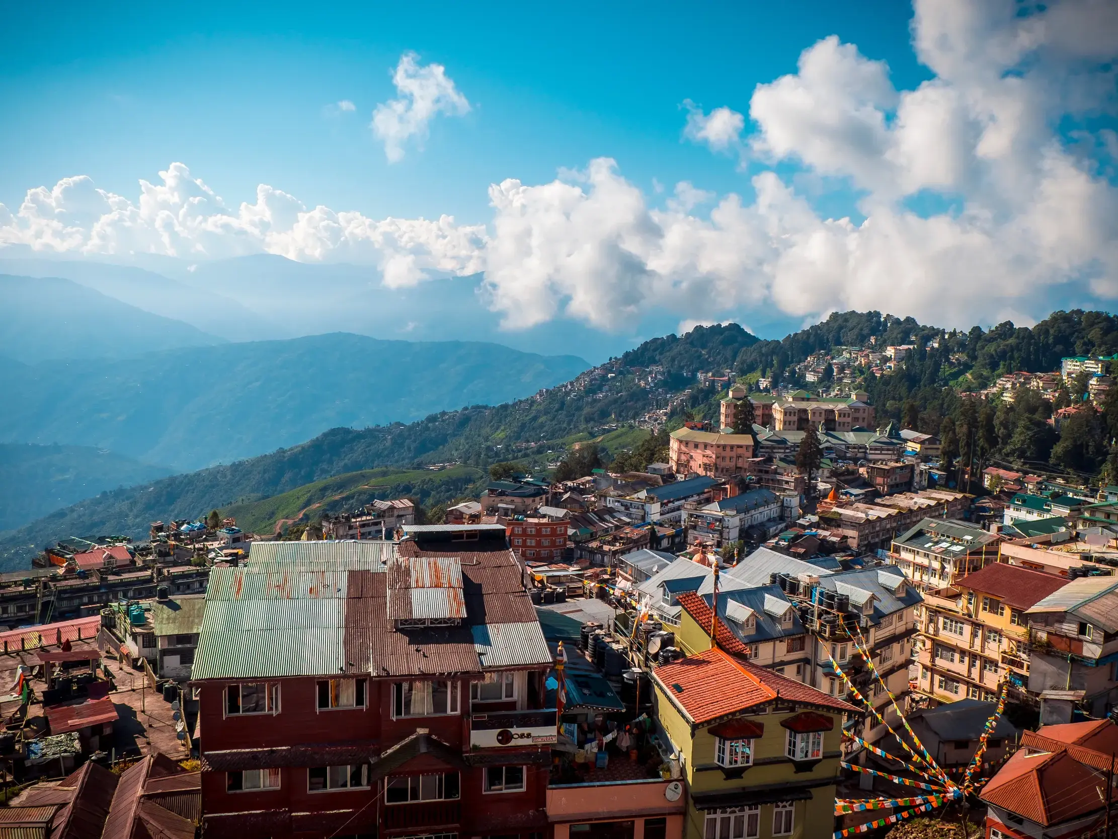 Panoramablick auf die bunten Häuser der Bergstadt Darjeeling, die sich an einen Hang im indischen Himalaya schmiegen.