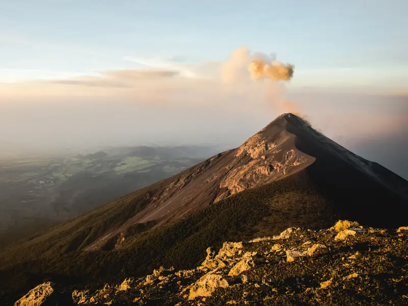 Der aktive Vulkan Fuego stößt bei Sonnenaufgang eine Rauchwolke aus, gesehen vom Gipfel des Acatenango während einer Trekkingreise.