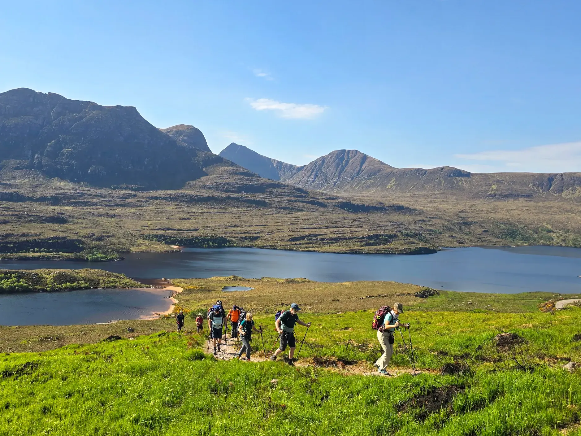 Wandergruppe auf einem Pfad in den North West Highlands mit Panoramablick auf einen tiefblauen Loch und die Berge von Wester Ross.