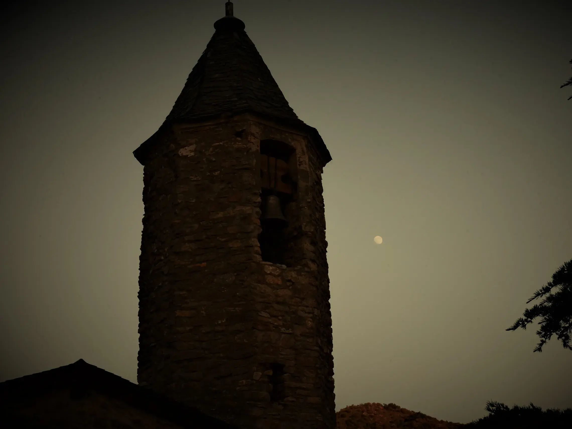 Steinerner Glockenturm einer Kapelle in einem Bergdorf in den spanischen Pyrenäen bei Vollmond in der Dämmerung.