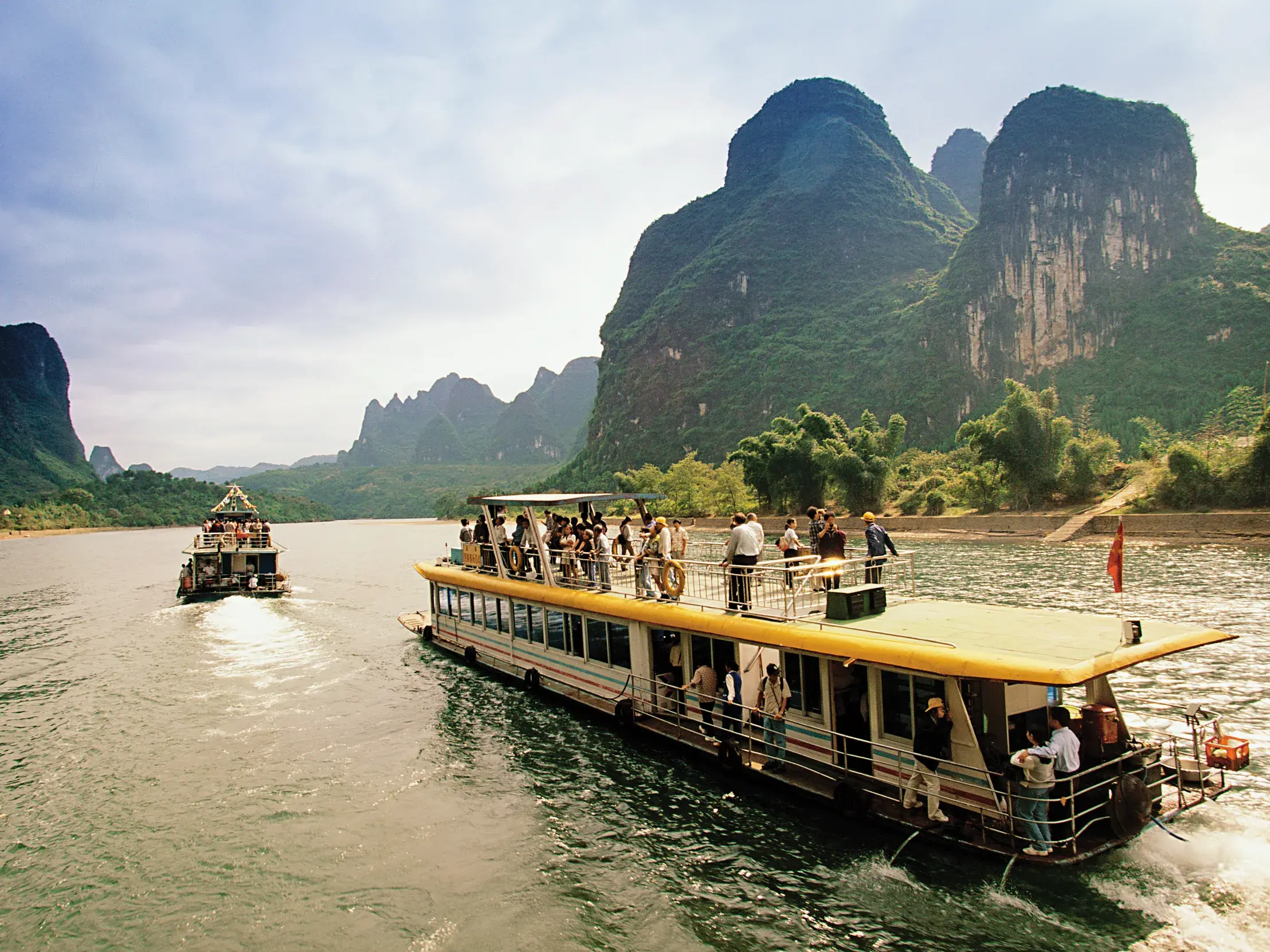 Eine Reisegruppe genießt die Bootsfahrt auf dem Li-Fluss durch die beeindruckende, grüne Karstlandschaft nahe Guilin.