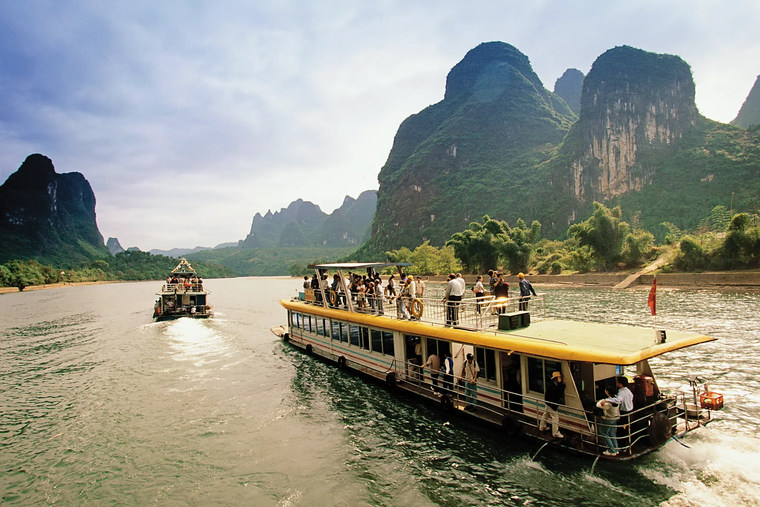 Eine Reisegruppe genießt die Bootsfahrt auf dem Li-Fluss durch die beeindruckende, grüne Karstlandschaft nahe Guilin.