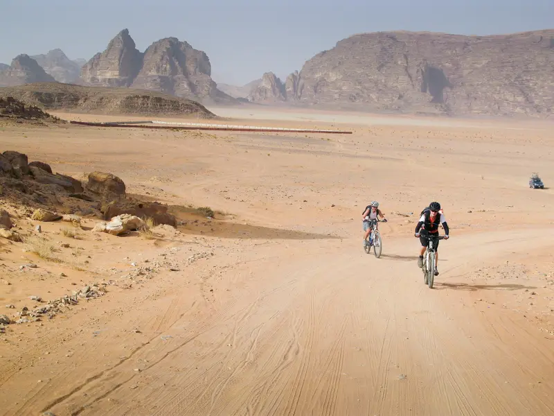 Zwei Mountainbiker auf einer geführten Radreise auf einem sandigen Offroad-Pfad durch die Wüste von Wadi Rum in Jordanien.