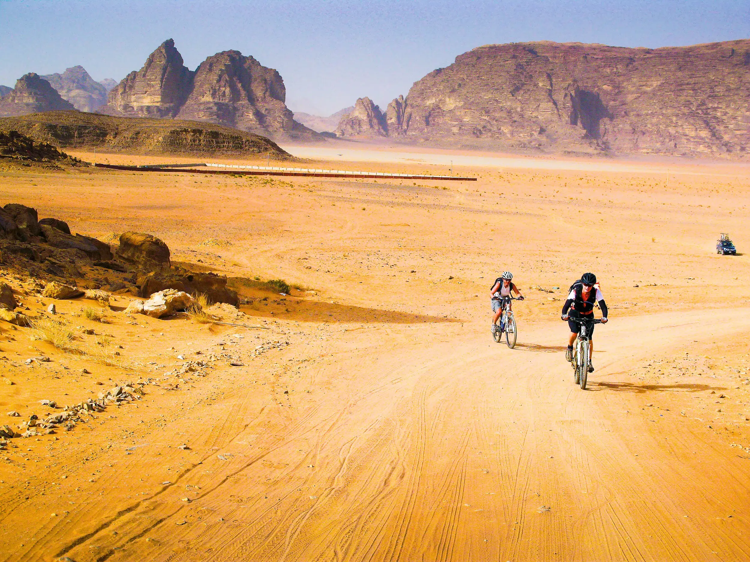 Zwei Mountainbiker einer Reisegruppe auf einem Sandweg durch die spektakuläre Felsenwüste des Wadi Rum in Jordanien.
