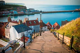 Blick über die steilen 199 Stufen hinab auf die Dächer und den Hafen des Küstenstädtchens Whitby in Nordengland.