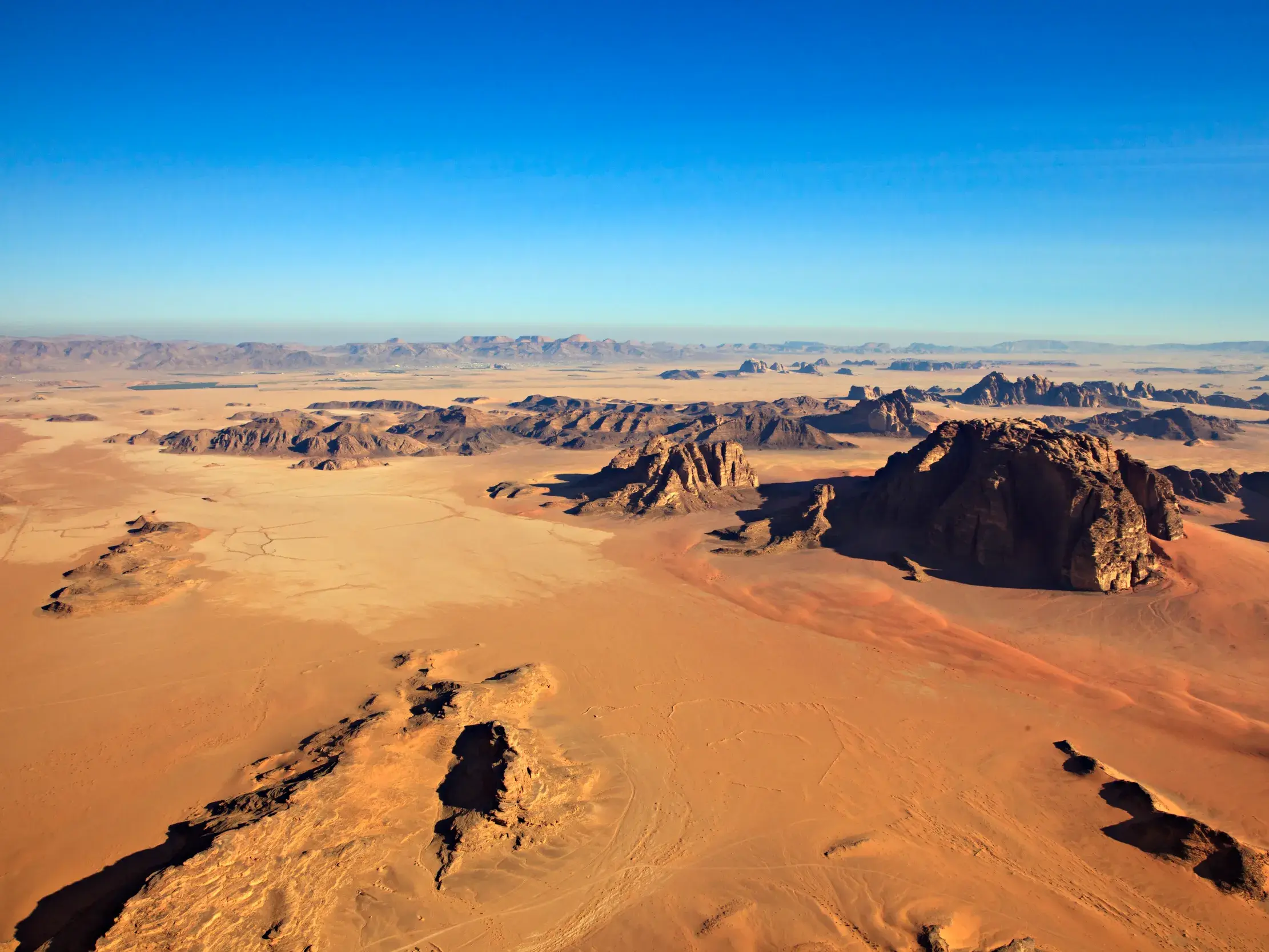 Weite Wüstenlandschaft des Wadi Rum in Jordanien mit roten Sanddünen und bizarren Felsformationen unter klarem blauem Himmel.