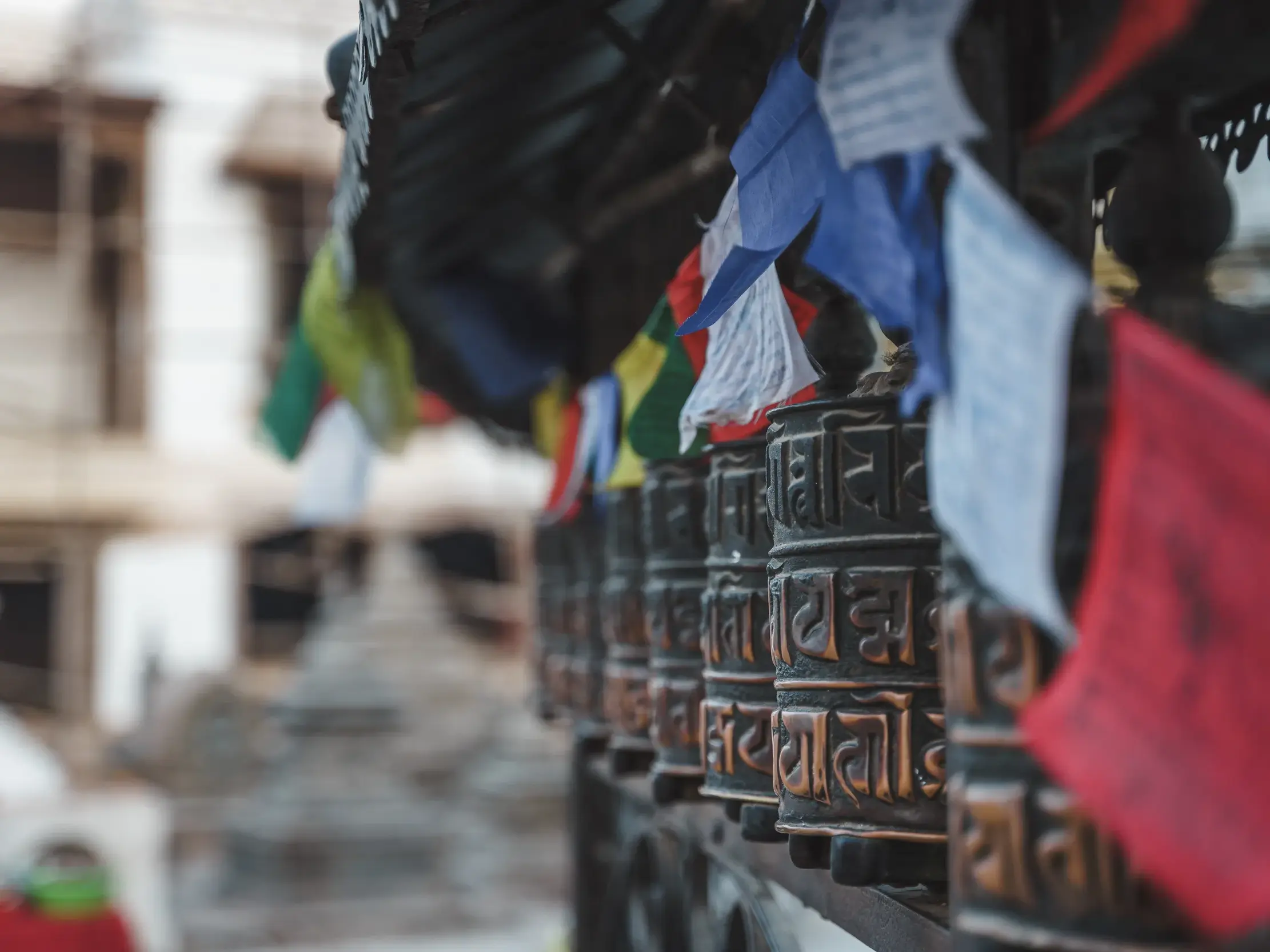 Nahaufnahme von Gebetsmühlen mit Sanskrit-Inschriften und Gebetsfahnen bei einer Trekkingreise in Kathmandu, Nepal.