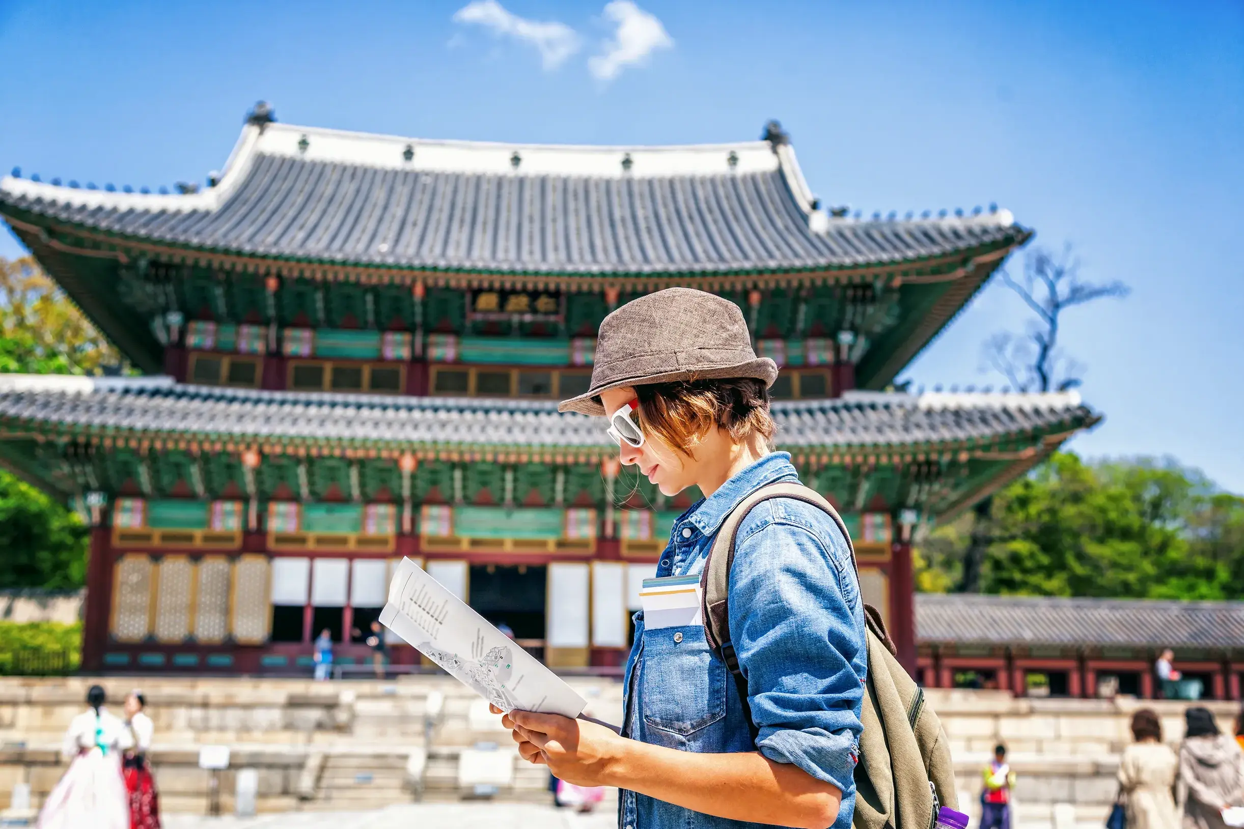 Ein junger Mann mit Hut auf einer Rundreise durch Südkorea studiert eine Karte vor dem Changdeokgung-Palast in Seoul.