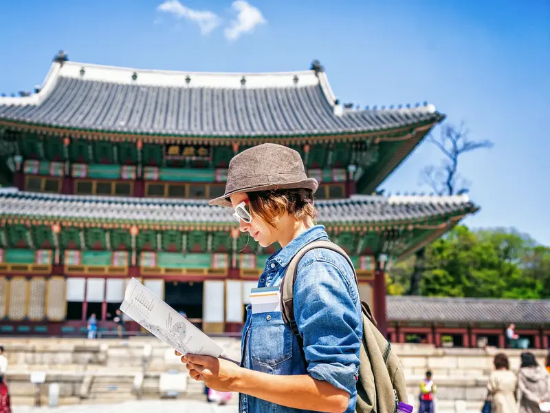 Ein junger Mann mit Hut auf einer Rundreise durch Südkorea studiert eine Karte vor dem Changdeokgung-Palast in Seoul.